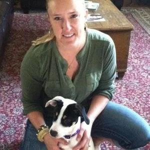 A woman sitting on a carpeted floor holding a black and white puppy.