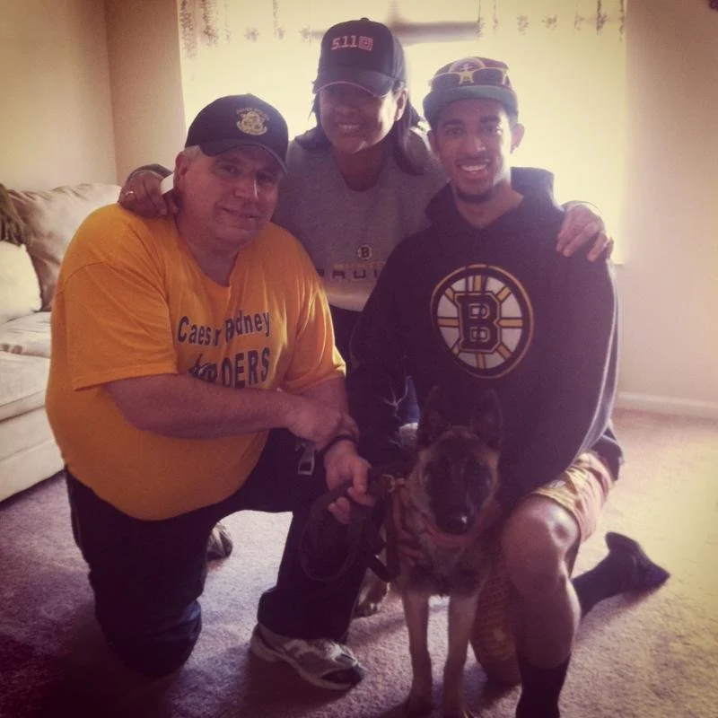 Three men and a dog pose together inside a living room, suggesting a family or friendly gathering.