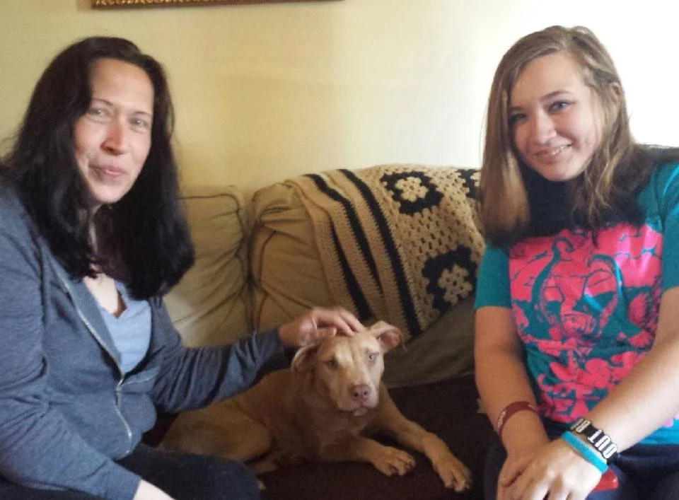 Two women and a brown dog sitting on a couch in a living room.