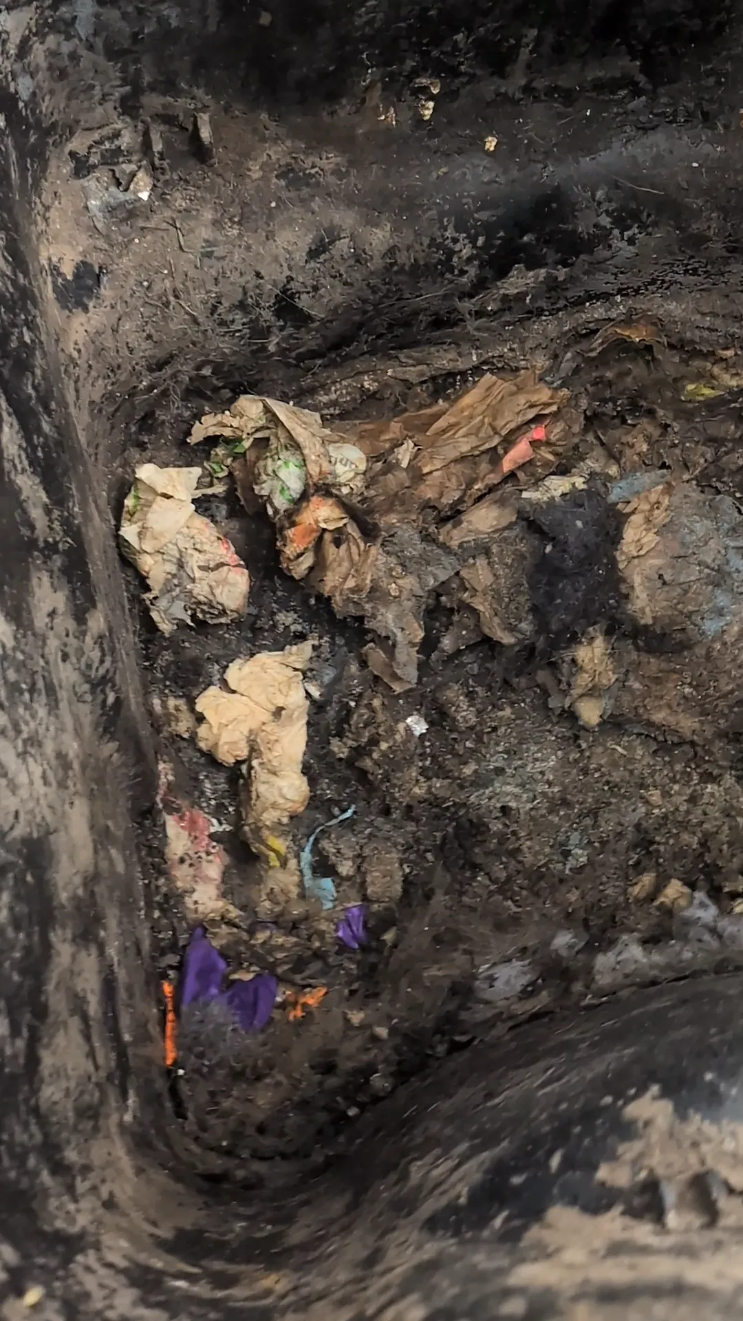 Close-up of a deep, dirty trash bin filled with crumpled paper, plastic, and other waste.