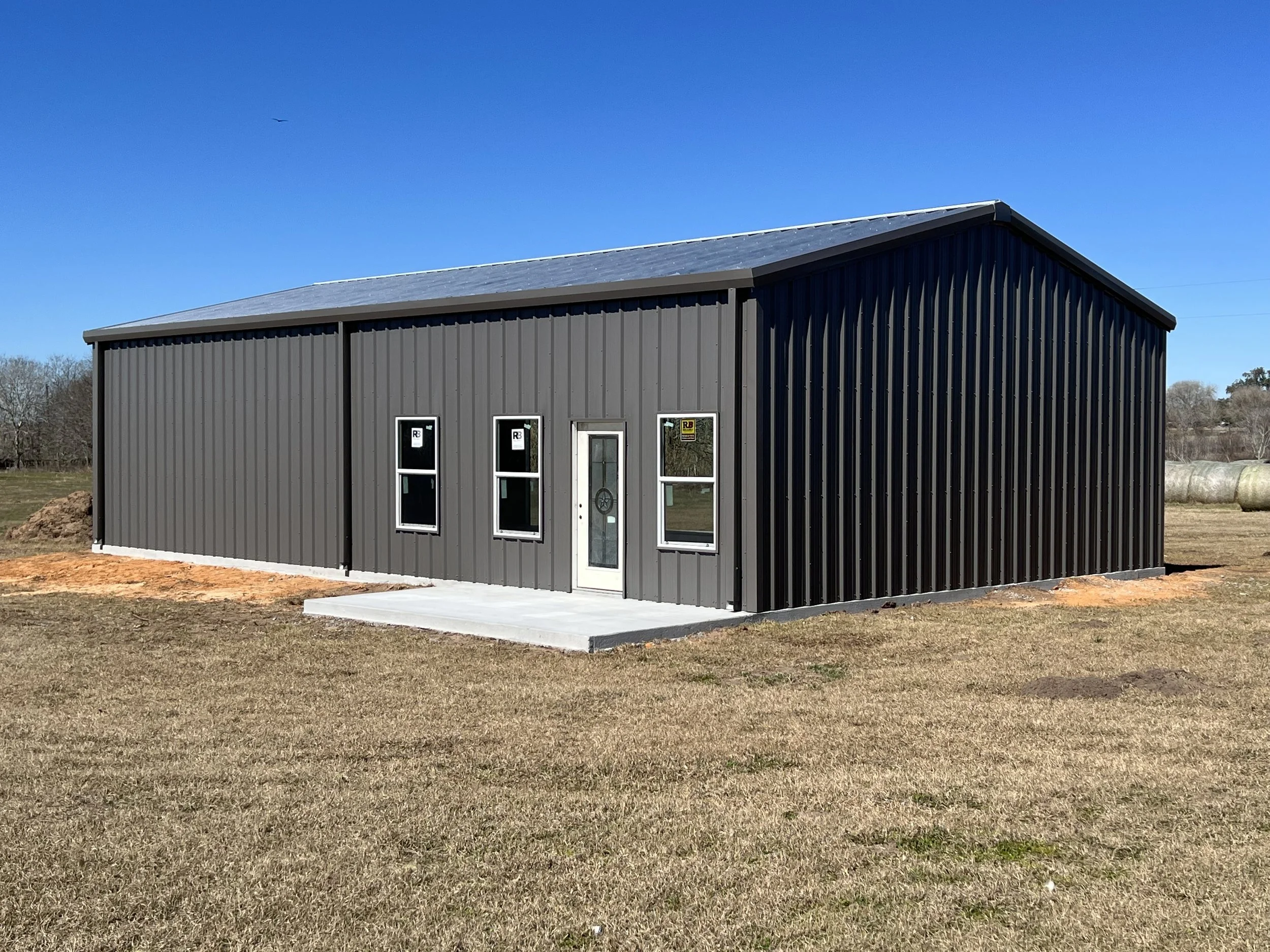 A gray metal barndominium, welded metal building kit with Charcoal Grey PBR Panel Walls, Galvalume PBR Panel Roof. Trim and gutter. rResidential doors and windows.