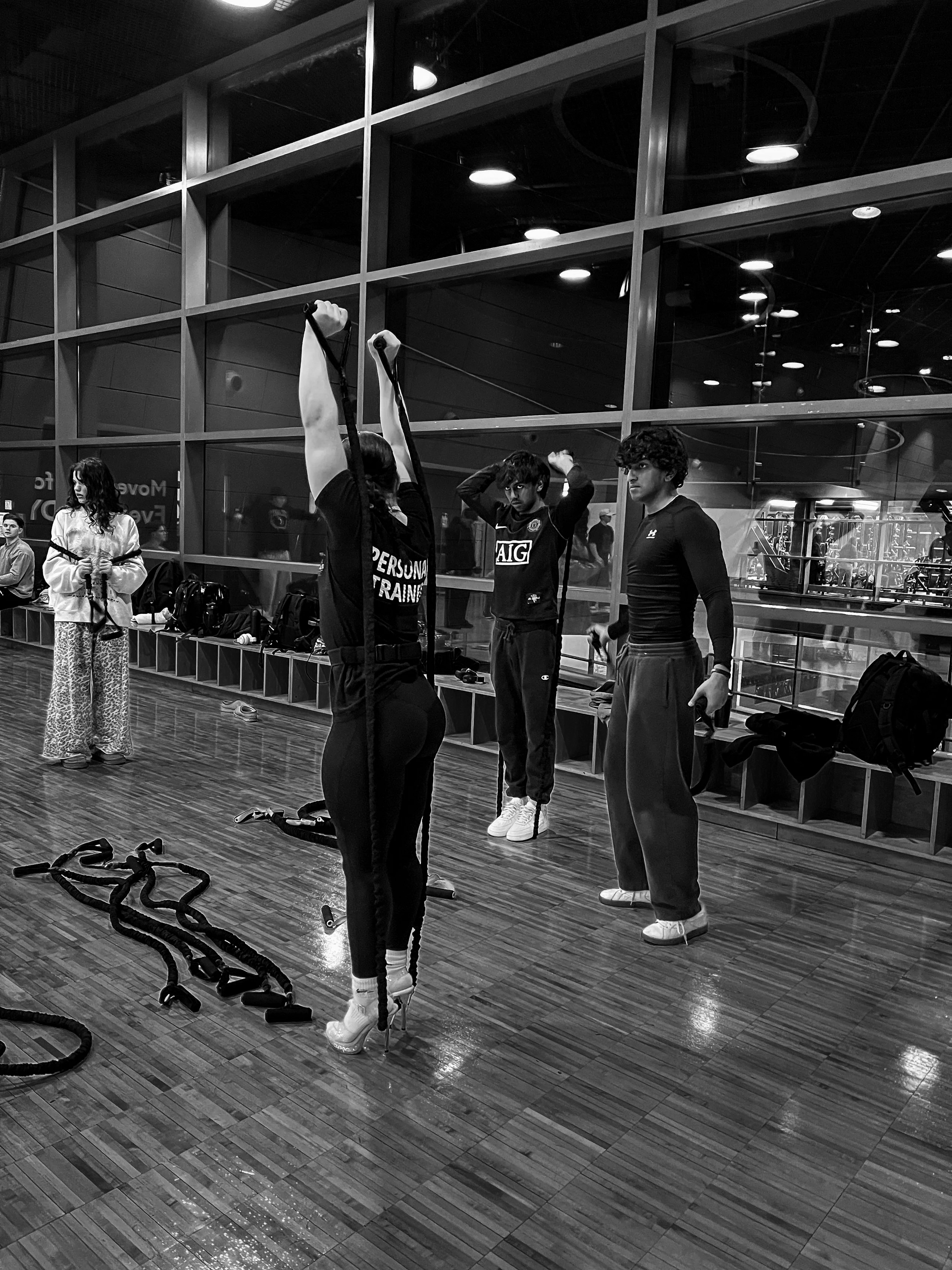 People stretching and preparing for exercise at a gym, with fitness equipment and mirrors in the background.