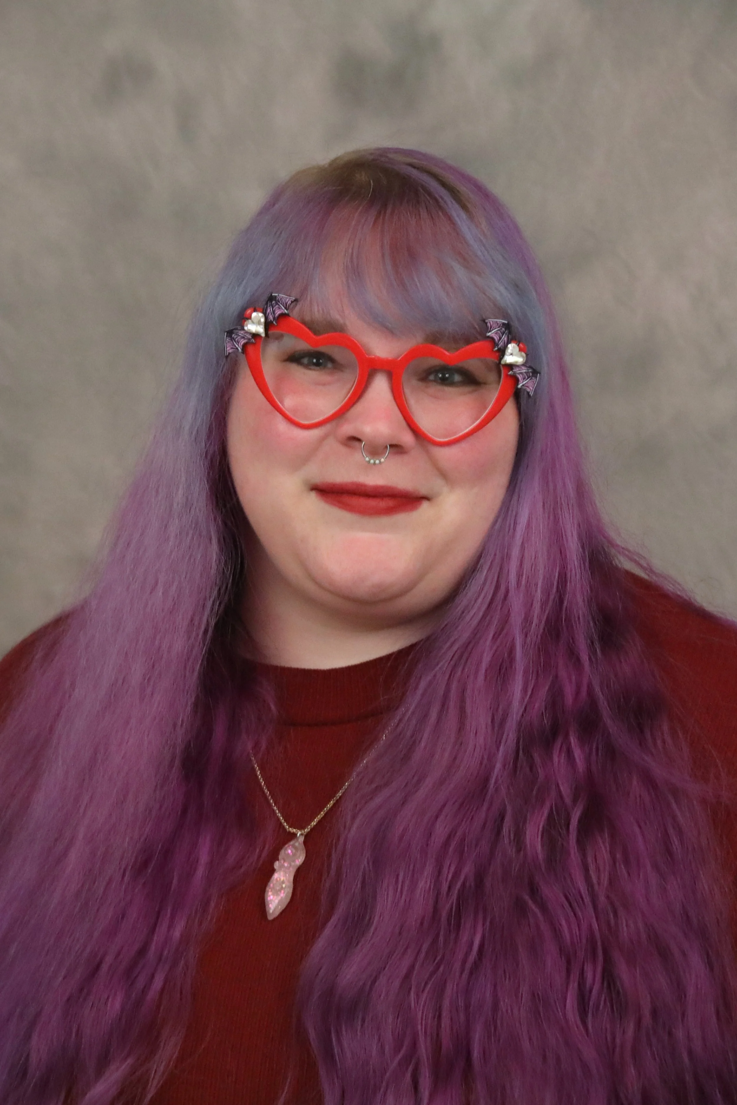 Image of a woman with purple hair wearing red heart glasses with bats on them.