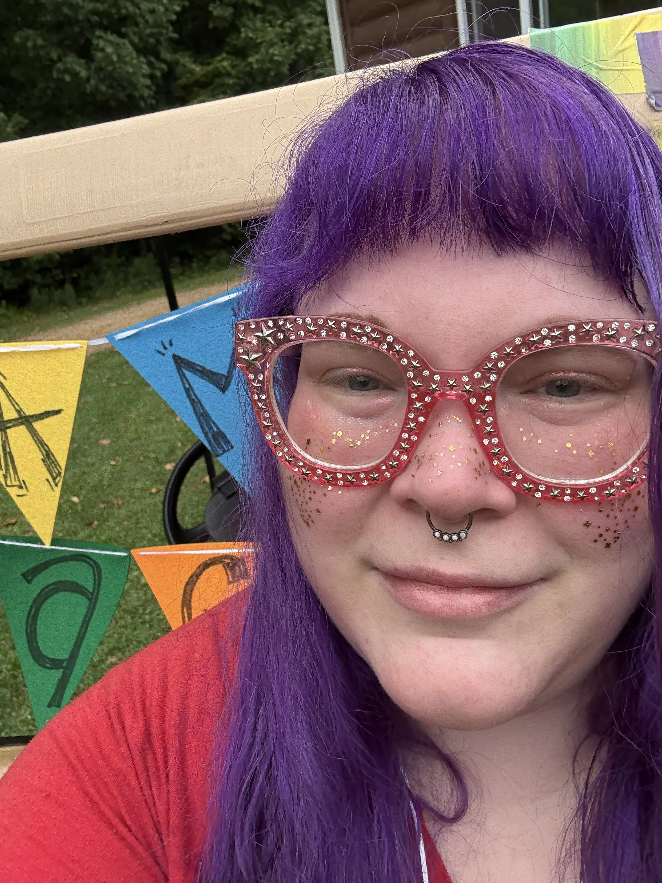 Image of a woman with purple hair, large pink glasses, and glitter freckles.