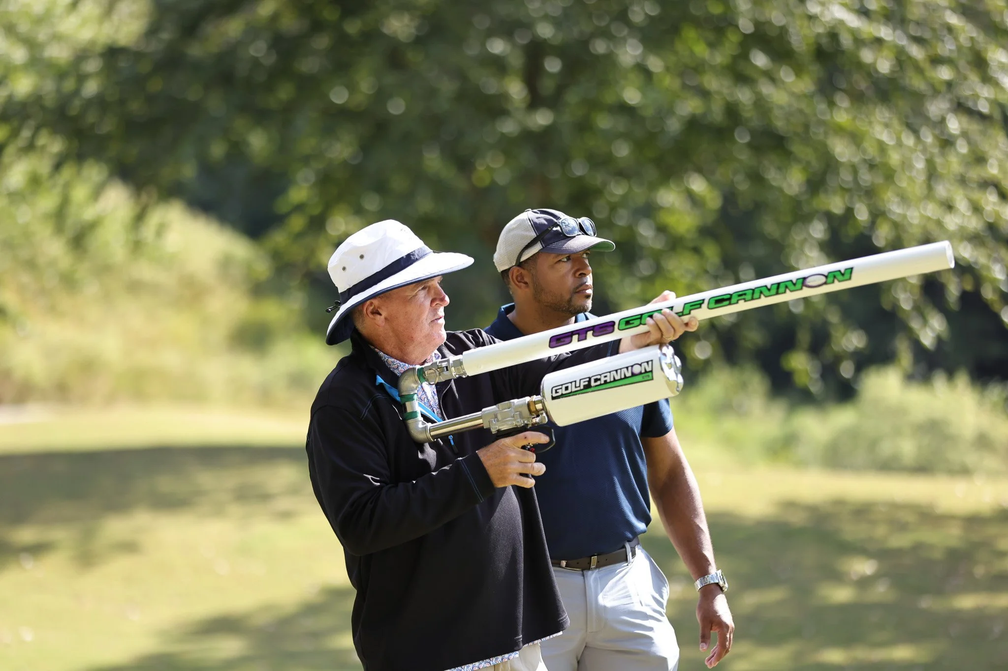 Two men on a golf course, one older and one younger, with the older man holding a golf launch monitor device.