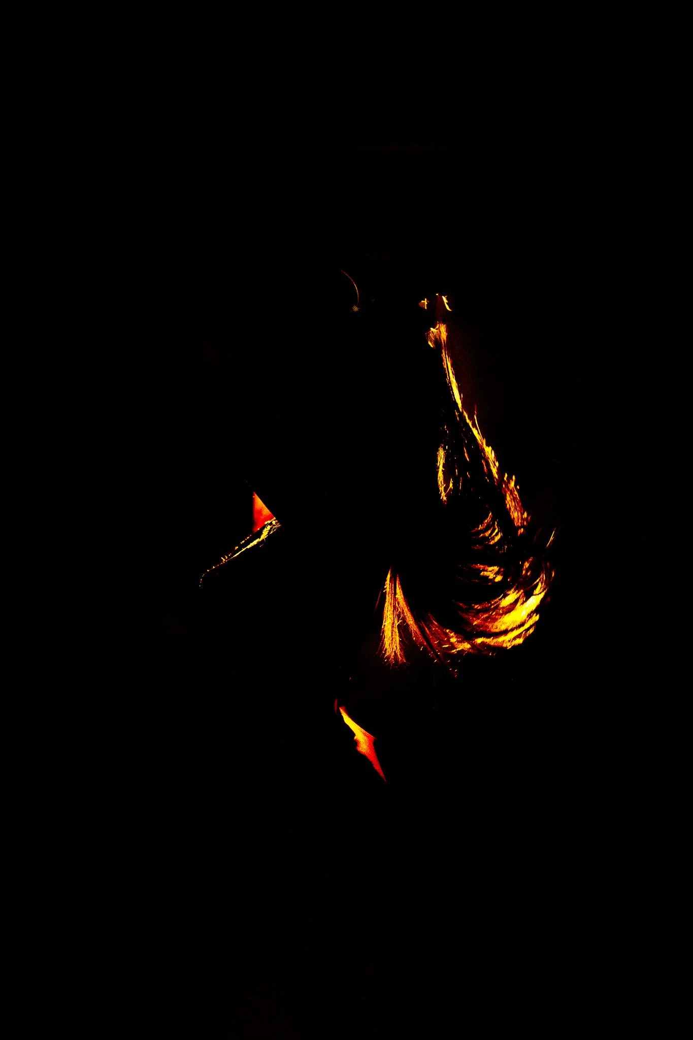Close-up of a person holding a sparkler at night, with bright orange sparks illuminating their hand and hair against a dark background.