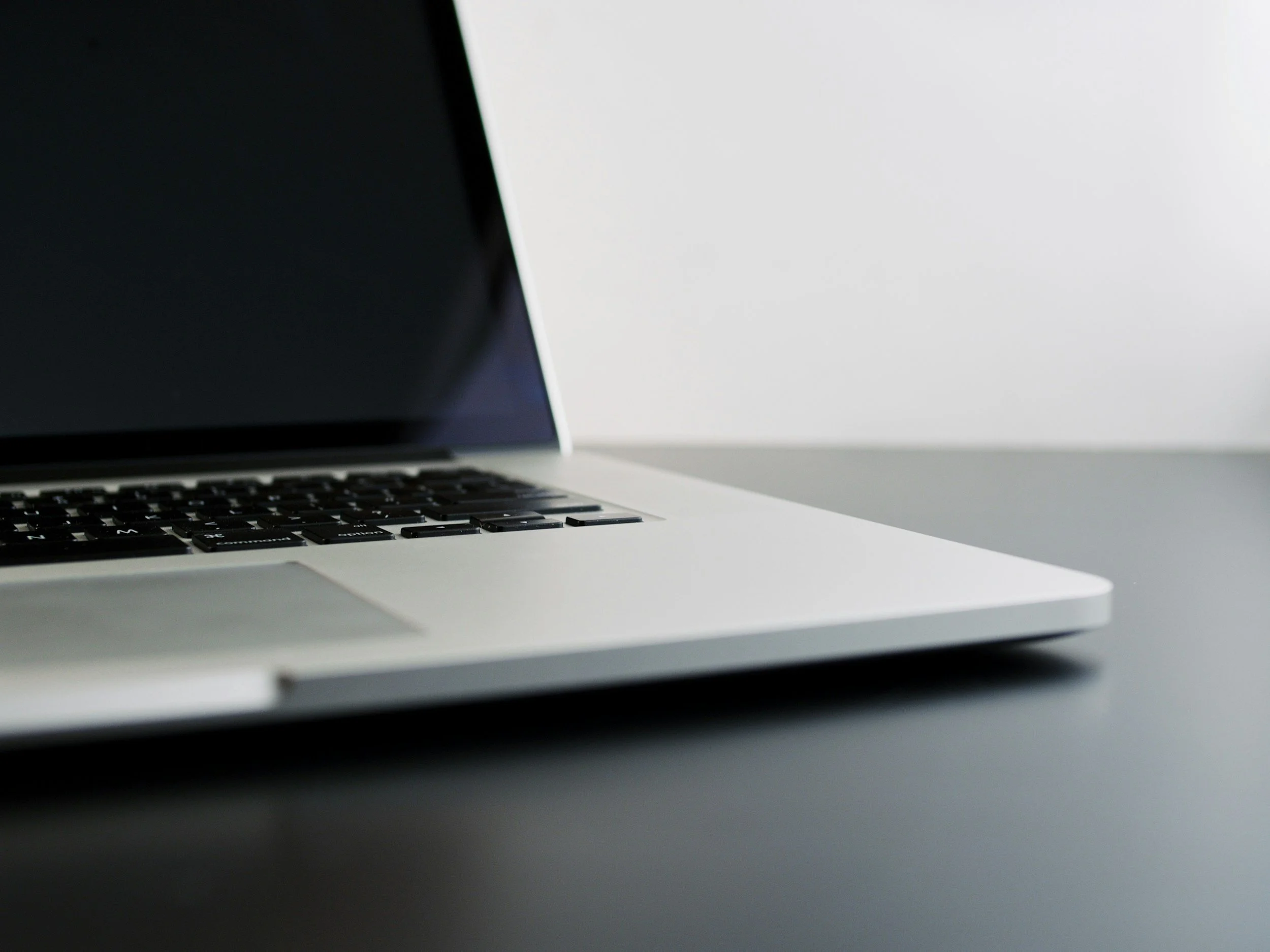 Close-up of a silver laptop keyboard and partially open lid on a light surface against a plain background.