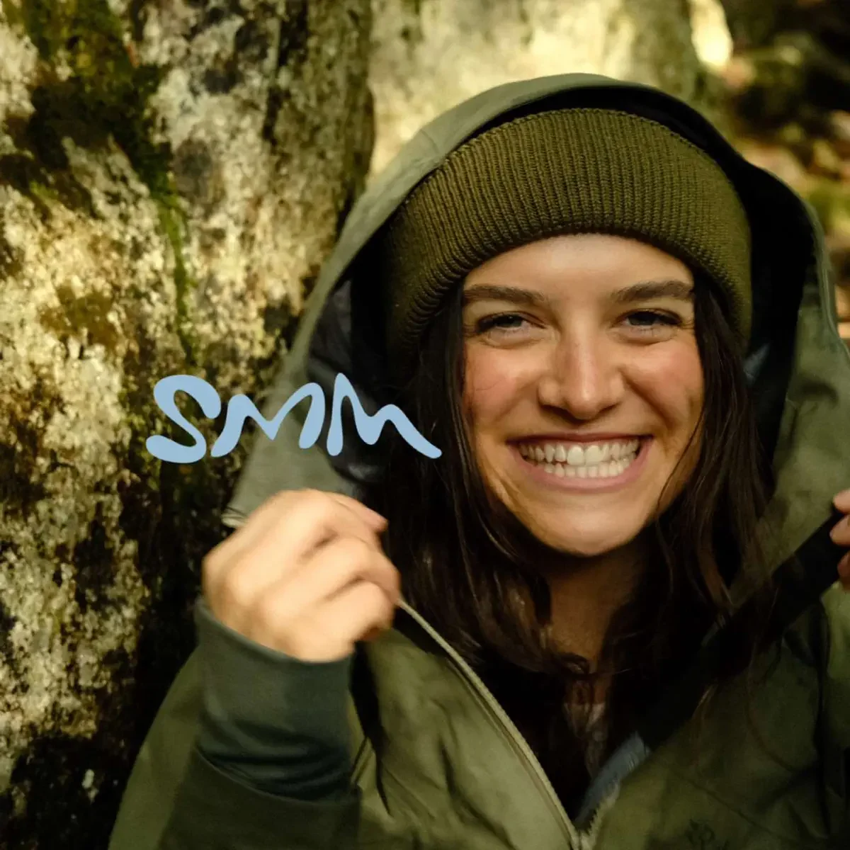 A woman outdoors smiling and holding a signature marker near a moss-covered rock.