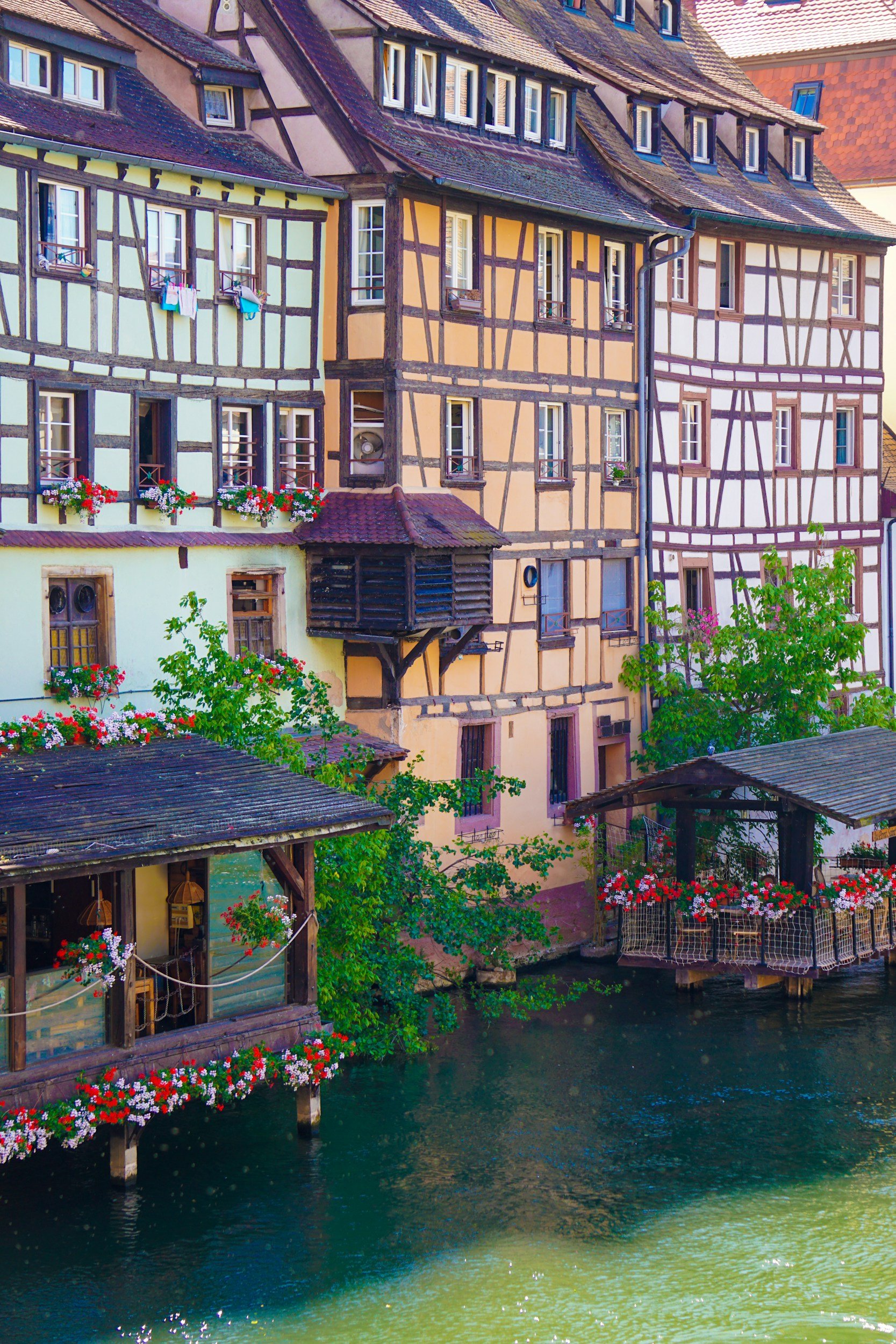 Colorful, traditional half-timbered houses along a river, with flower boxes on the windows and laundry hanging outside, in a picturesque European village.