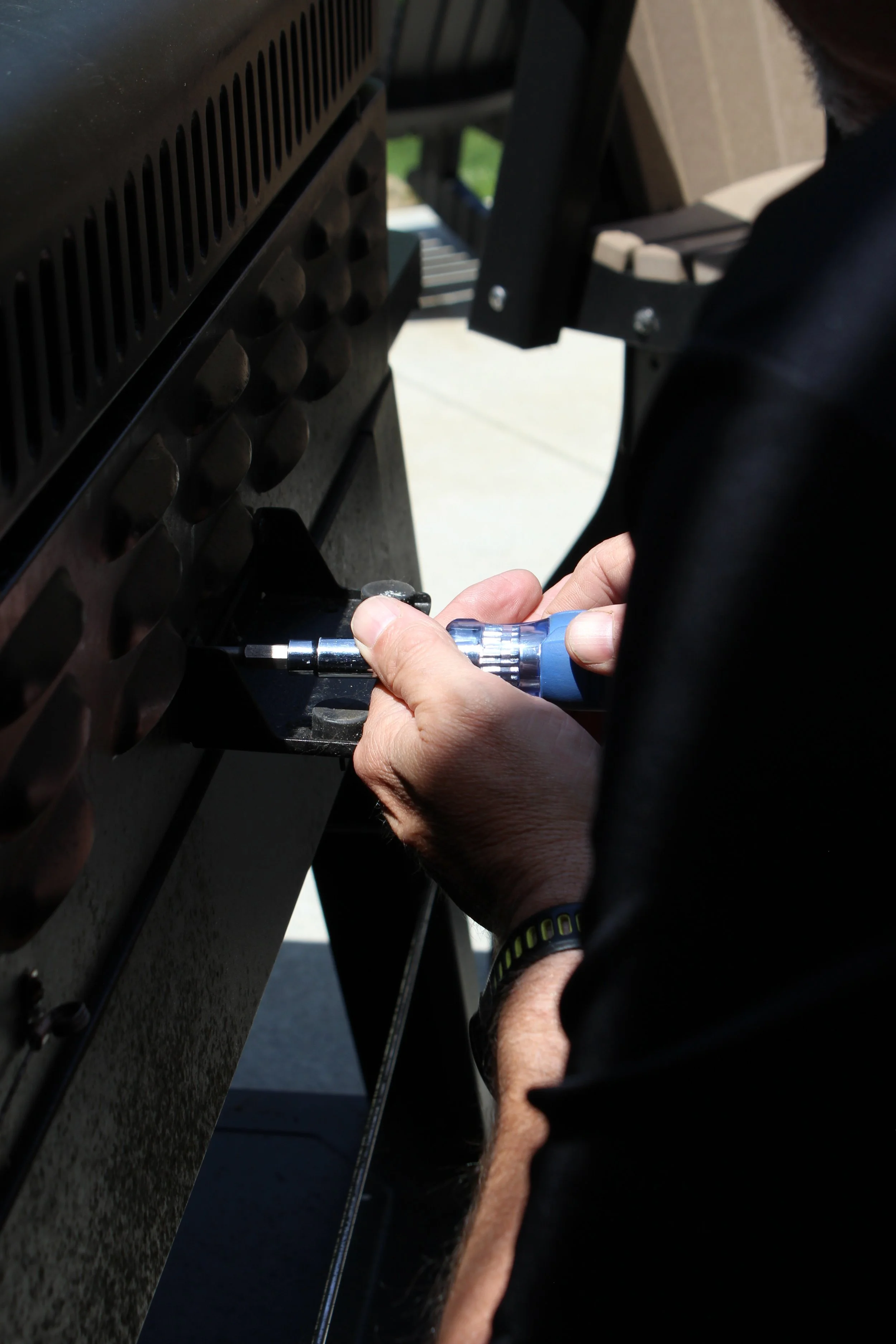 A person using a screwdriver to fix or assemble a grill or stove outdoors.