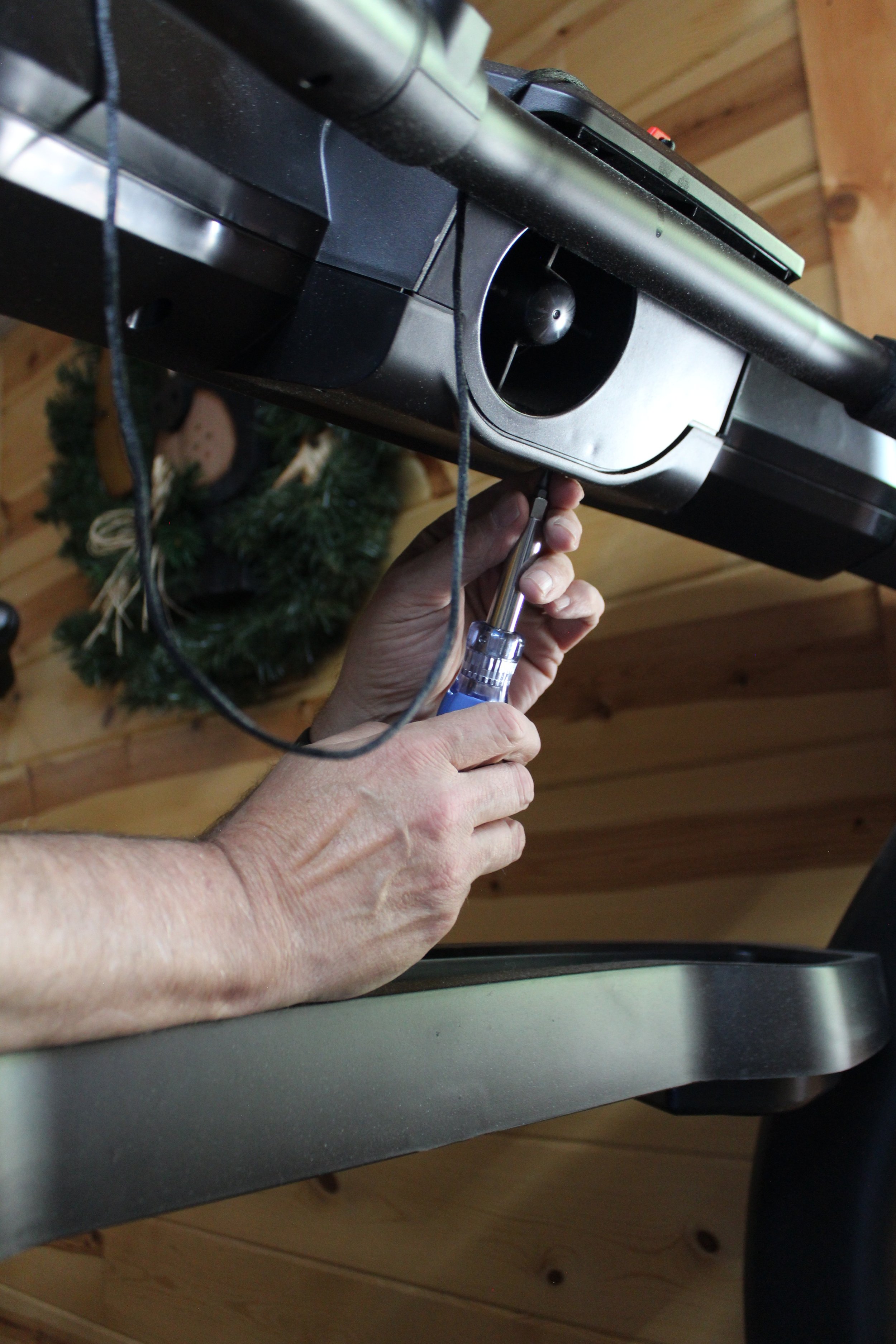 A person is using a screwdriver to work on a treadmill in a home gym.