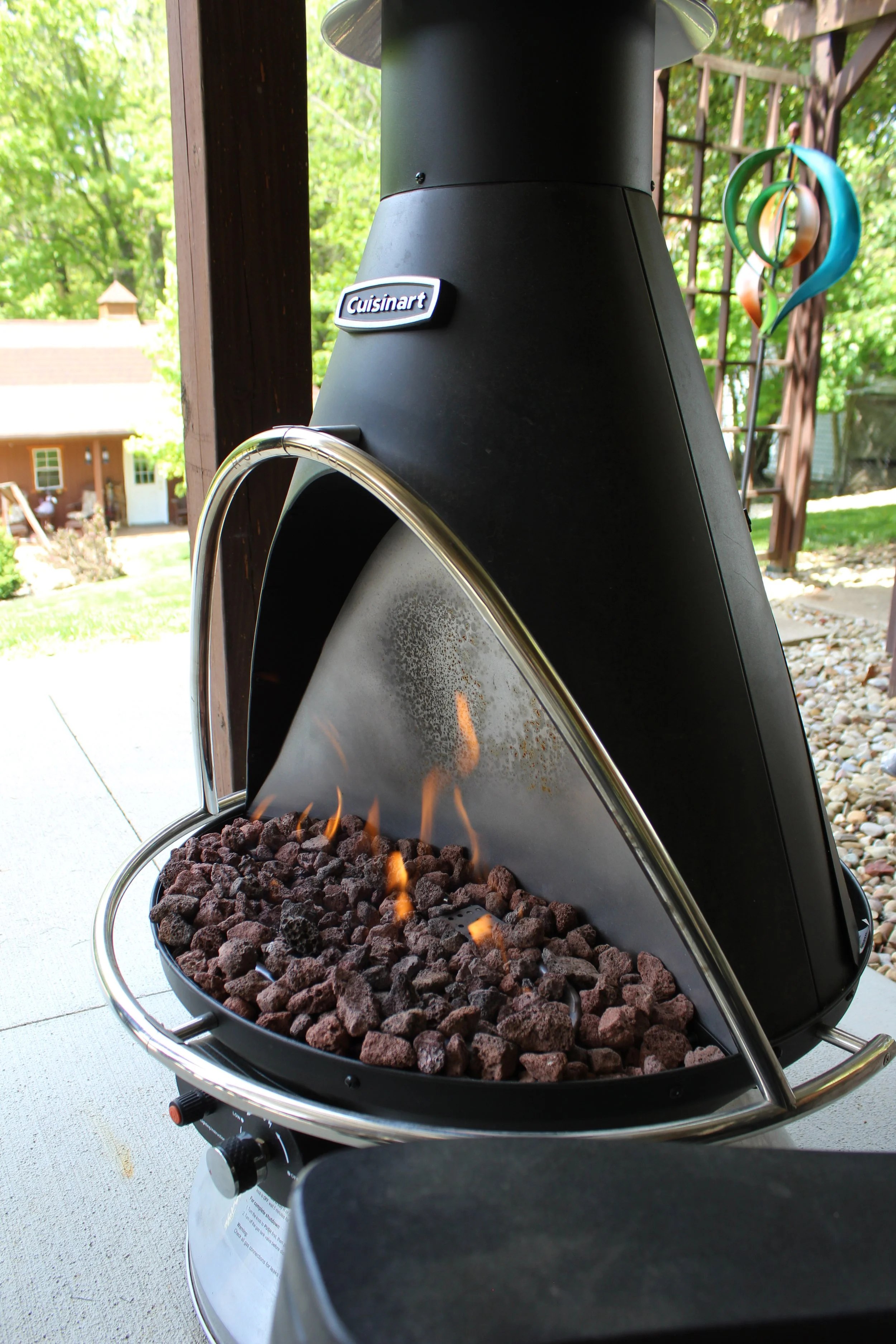 A Cuisinart charcoal grill with flame and charcoal inside, outdoors on a patio.