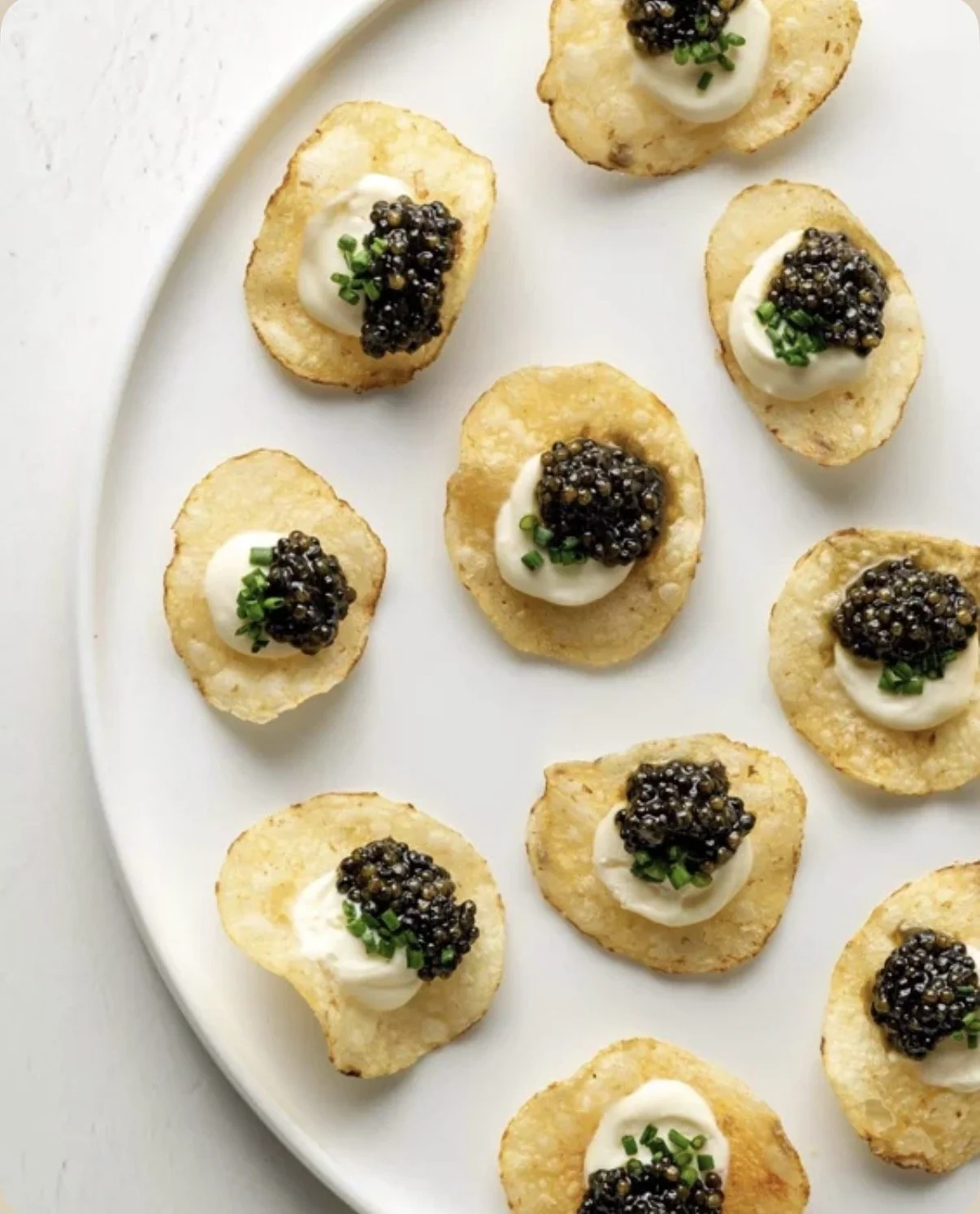 Potato chips topped with sour cream, caviar, and chopped green onions on a white plate.
