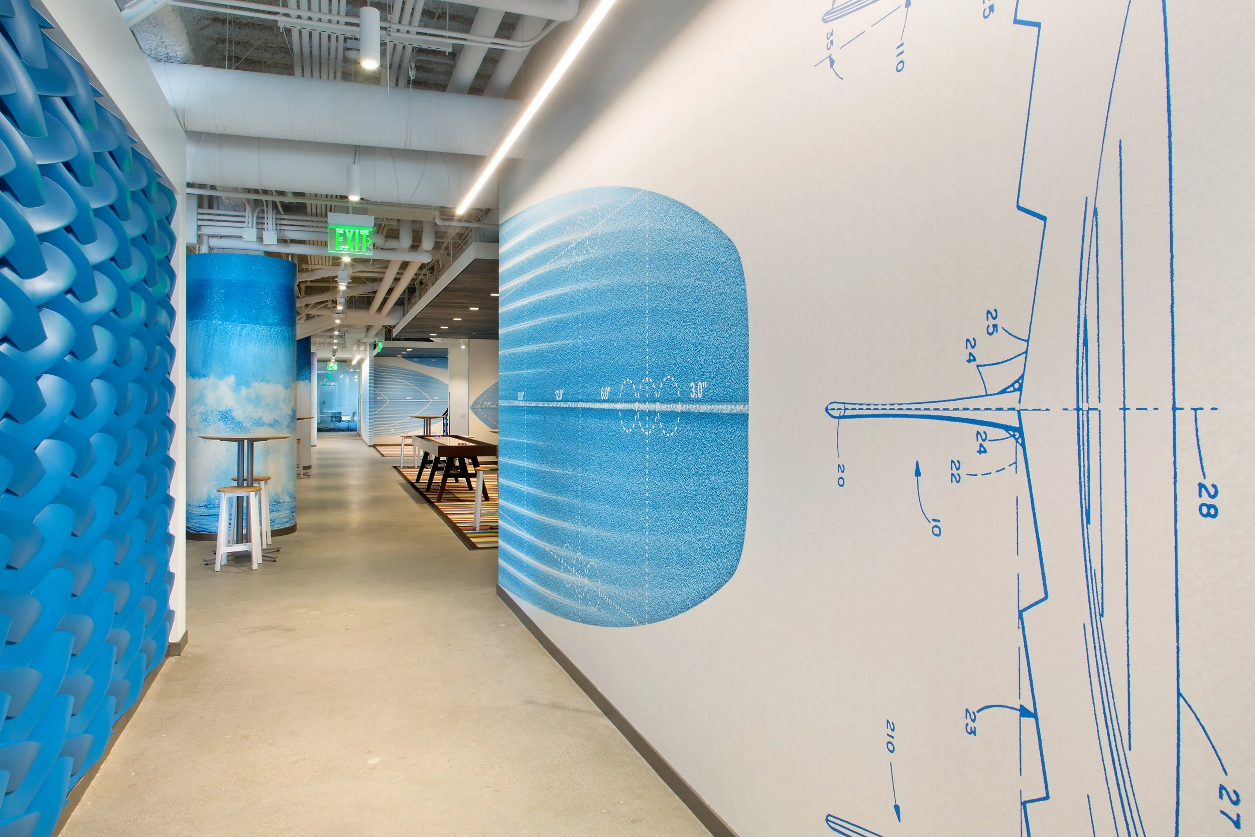A modern corridor with bright lighting, featuring walls decorated with blue wave and blueprint patterns, and a textured blue cylindrical column.