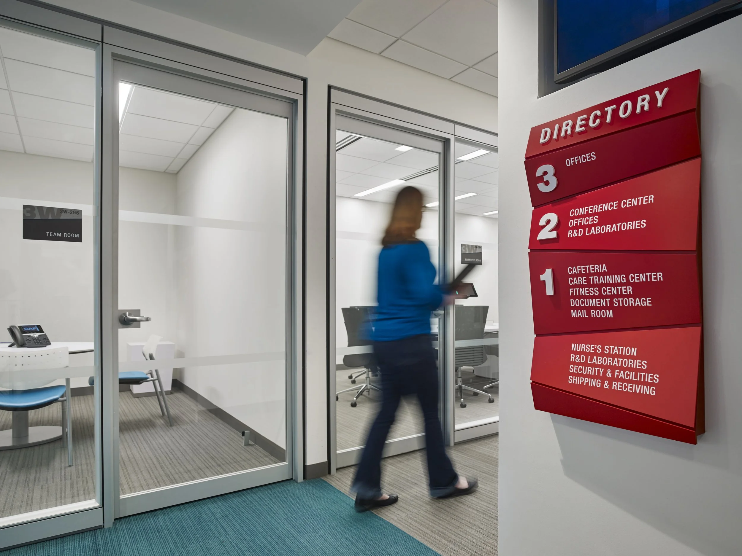 Woman walking past a red directory sign inside an office building. 