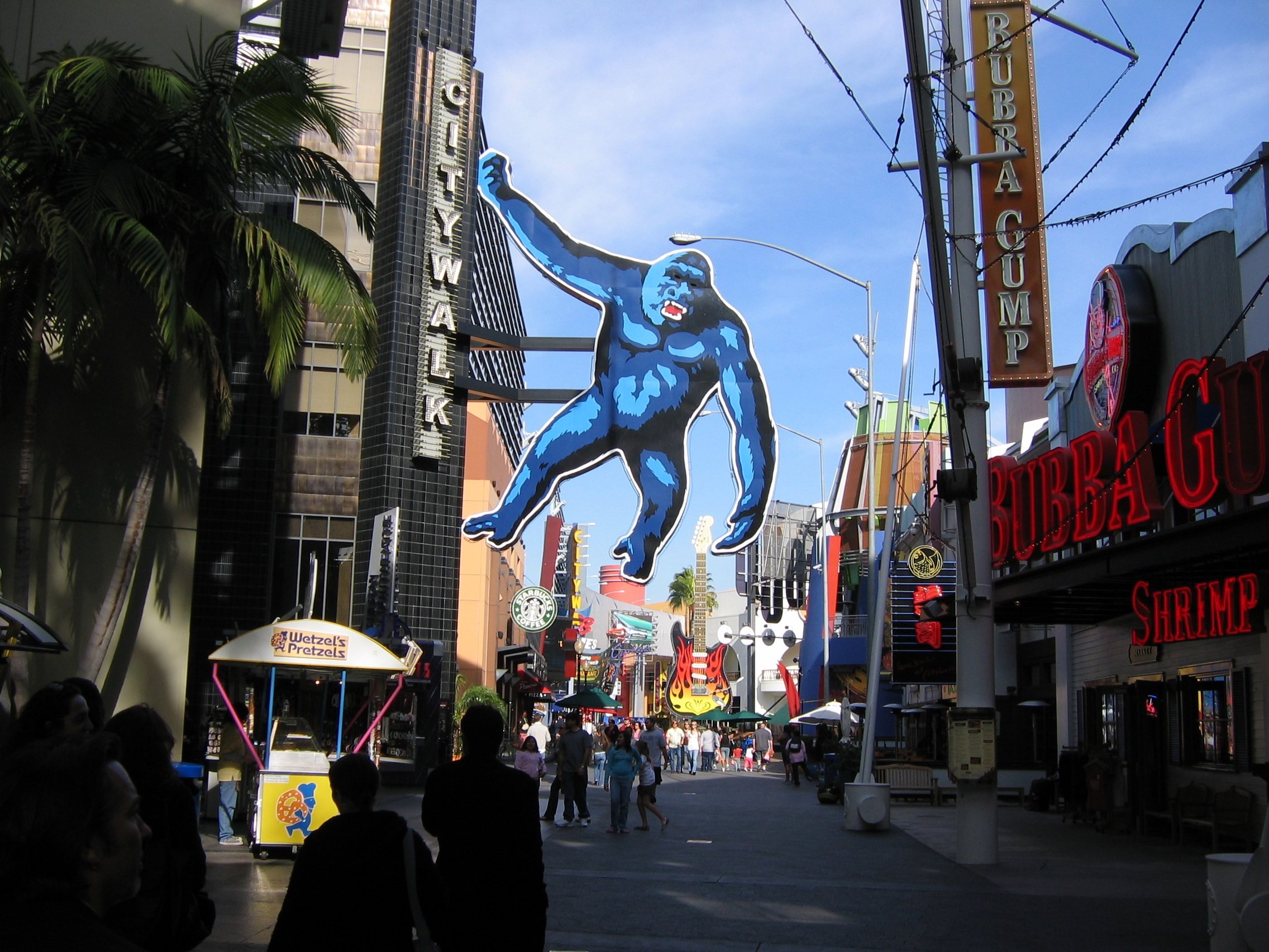Street scene on the Las Vegas Strip featuring neon signs, including a large blue gorilla, and crowds of people walking.