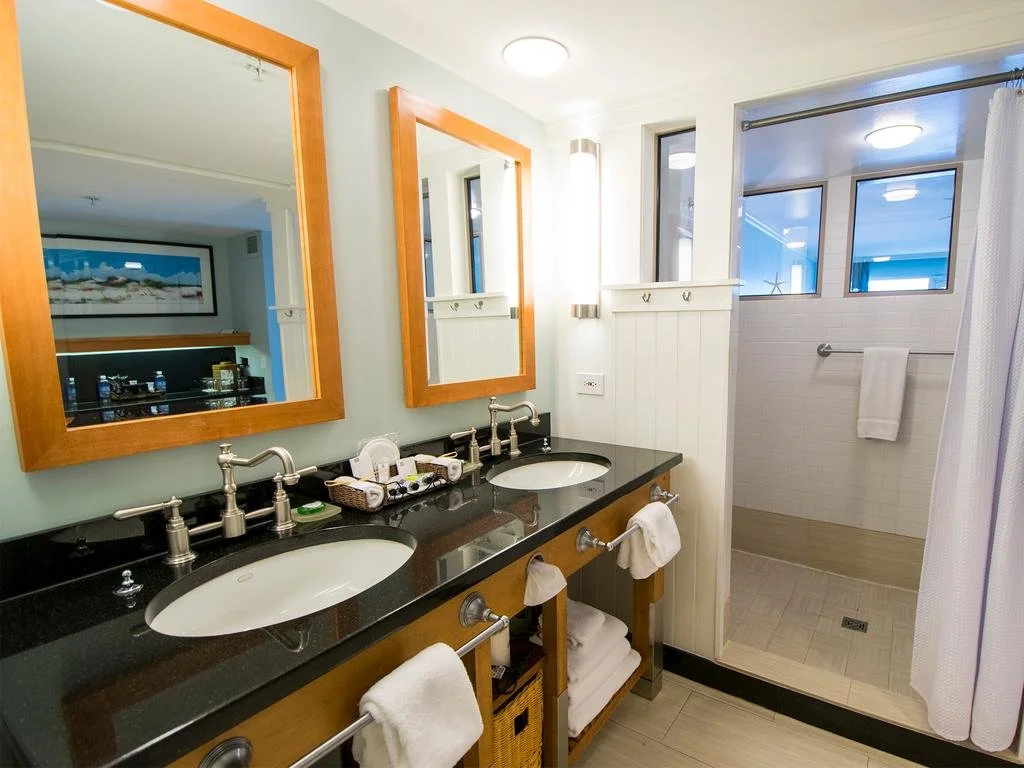 Bathroom with two sinks, large mirrors, and a walk-in shower with a window, white tiled walls, and a curtain.