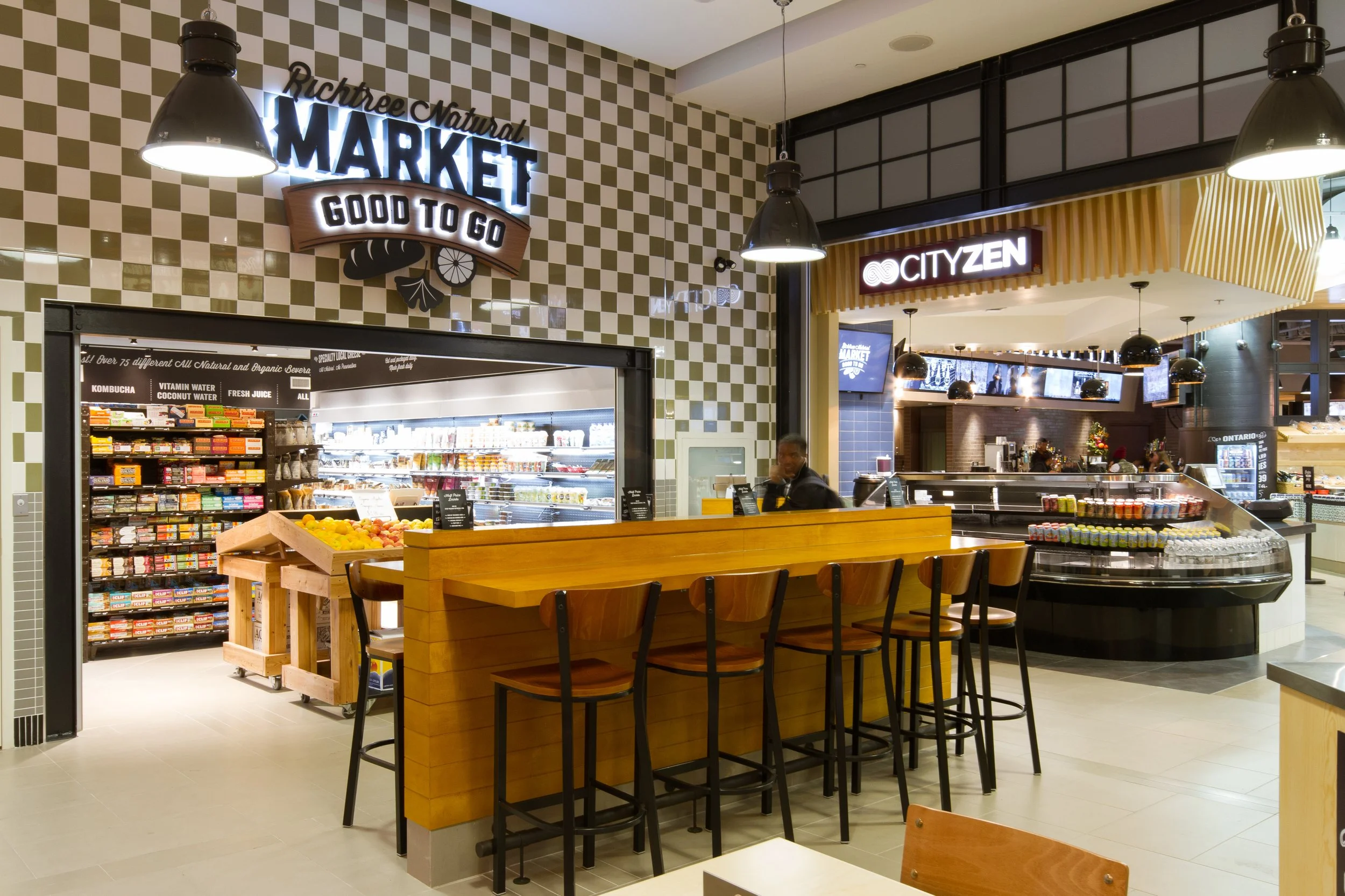 Interior of a modern grocery store with a seating area, checkered wall, and signs for 'Richtree Natural Market' and 'CITYZEN'.