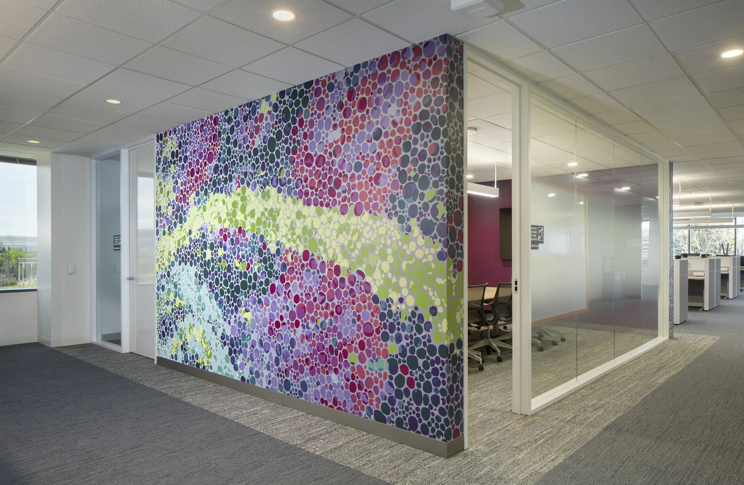 Interior of an office with a colorful, dotted-patterned wall, glass partitions, office chairs, and ceiling lights.