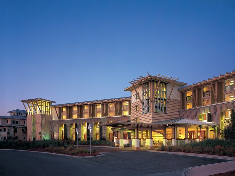 Modern multi-story residential or hotel building with illuminated windows at dusk, featuring unique architectural elements and a well-maintained front entrance.