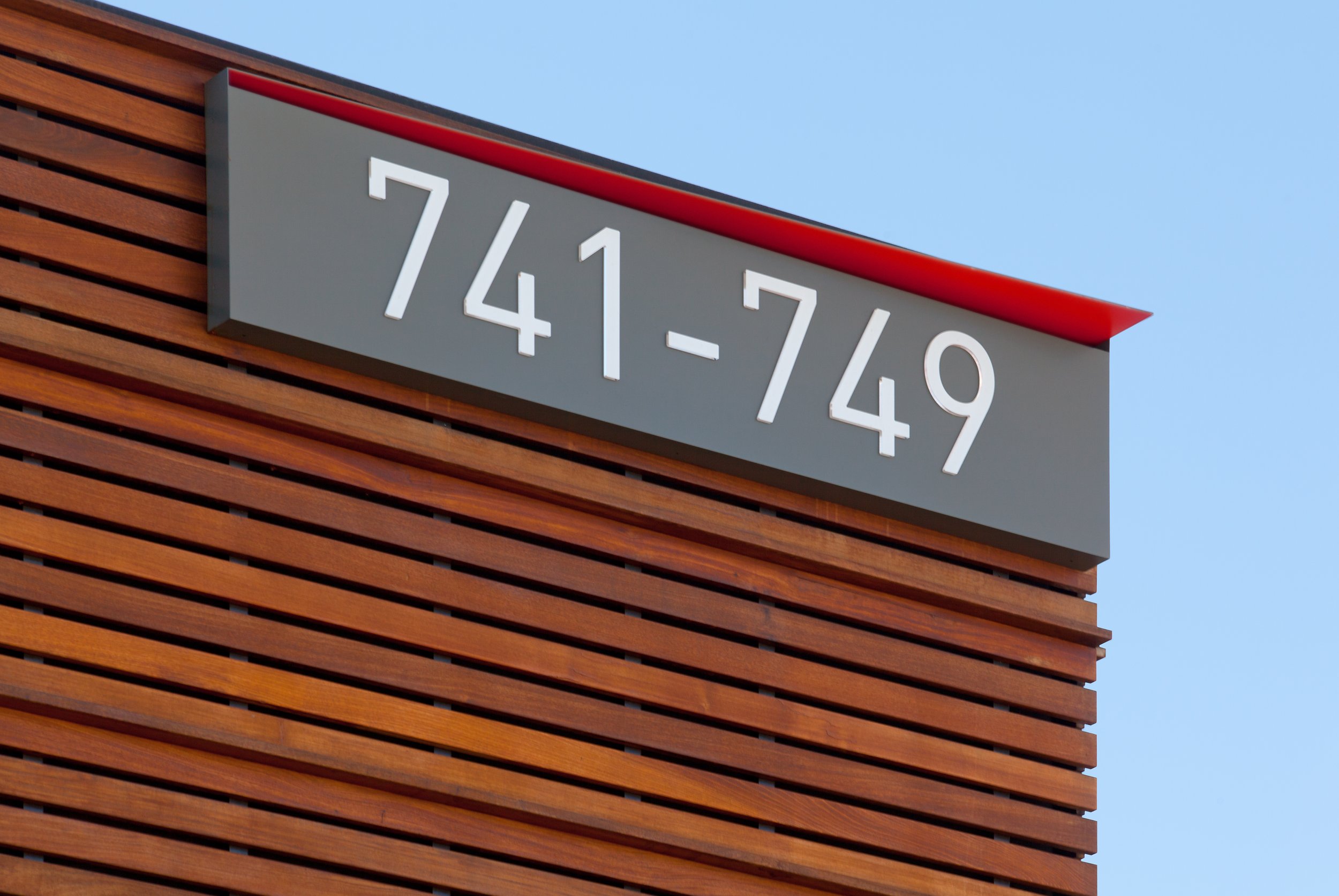 Close-up of a modern building with horizontal wooden slats and a gray sign displaying numbers 
