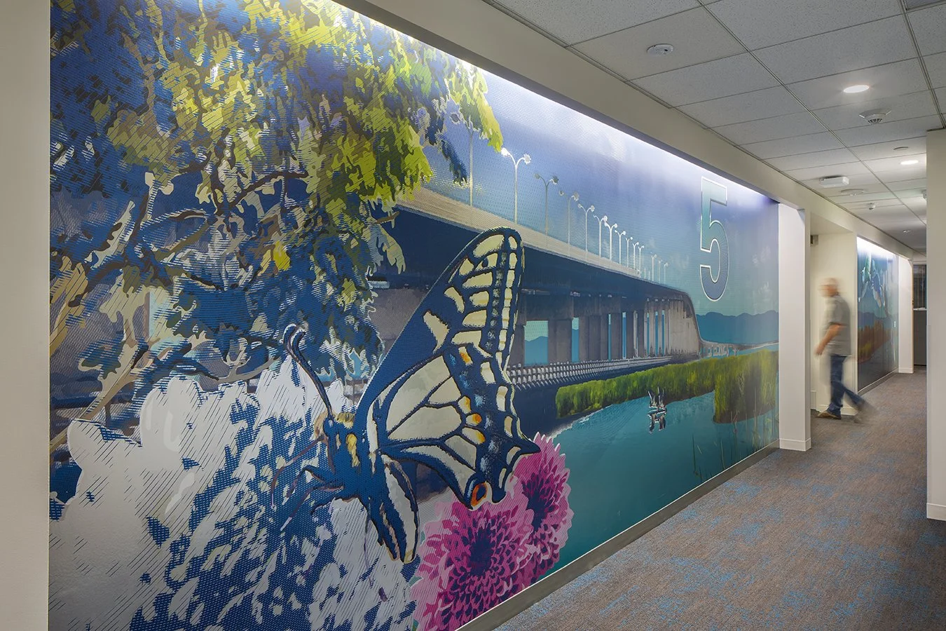 Colorful mural of a butterfly, bridge, and nature scene on office hallway wall.