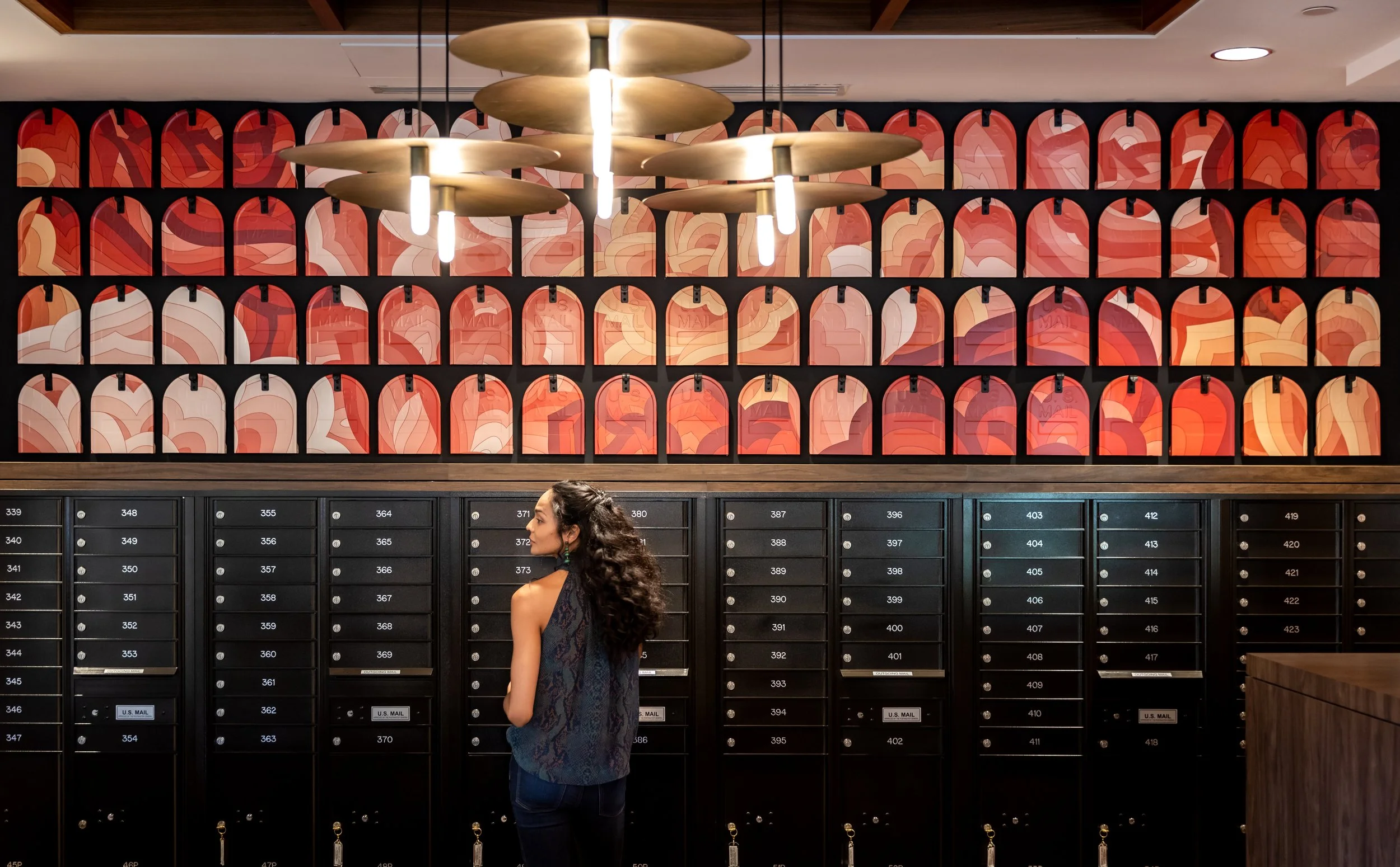 A woman standing in front of black mailboxes with a colorful abstract mural on the wall behind her.