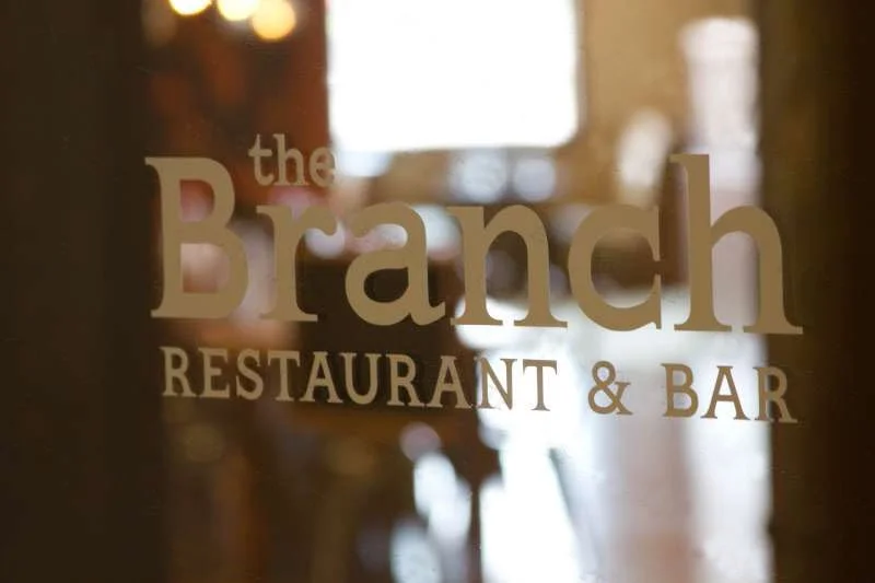 Sign for The Branch restaurant & bar with reflections on glass door or window.