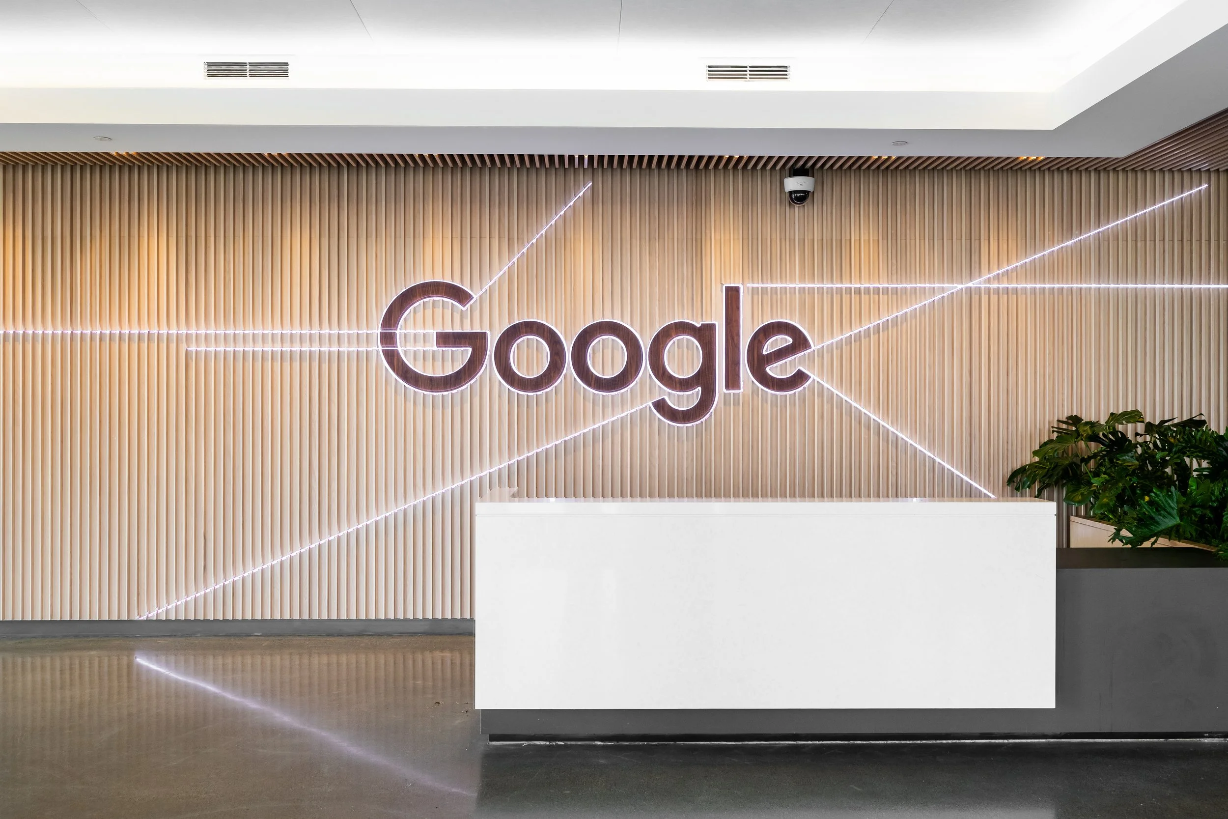 Interior view of a modern building with a wooden slat wall featuring neon lights forming the Google logo and a line graph.