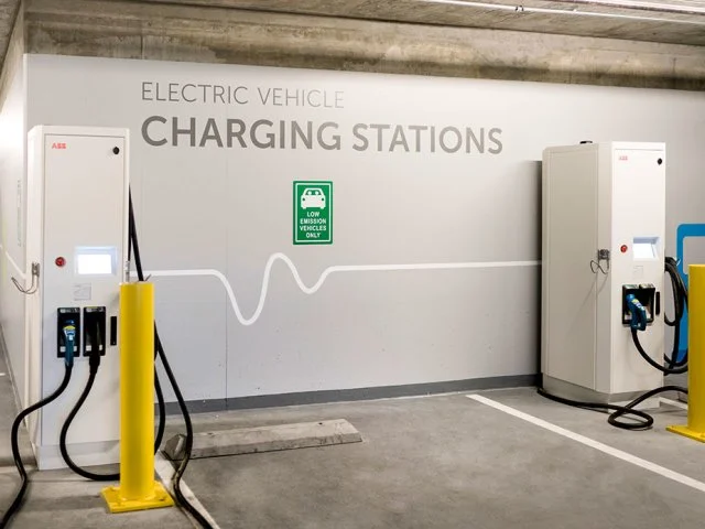Electric vehicle charging stations in a parking garage with a digital payment kiosk and a green sign indicating low emissions