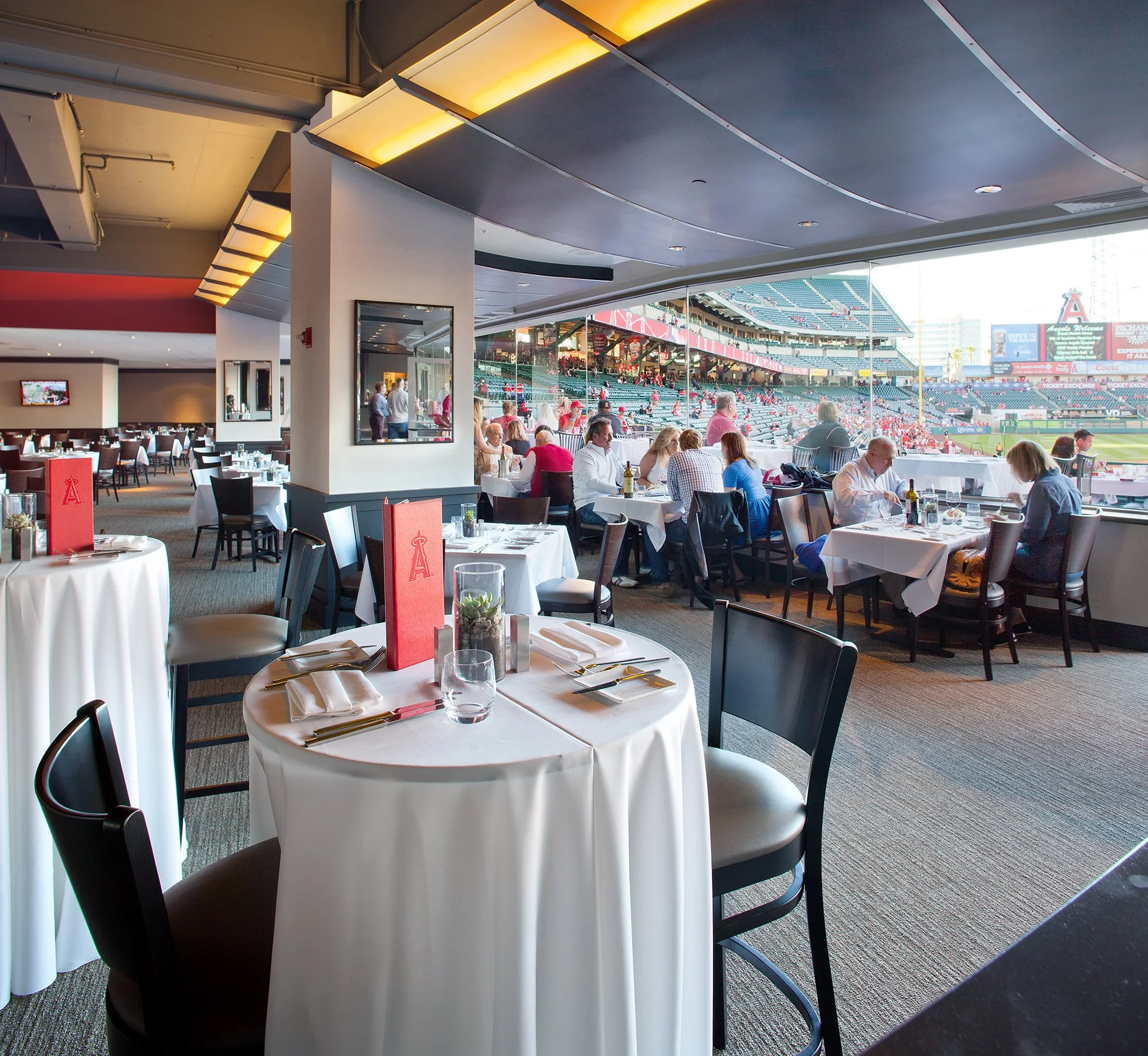 Interior of a Halo at Angel stadium Resturant, with tables set for dining and large windows overlooking the stadium seats and playing field.