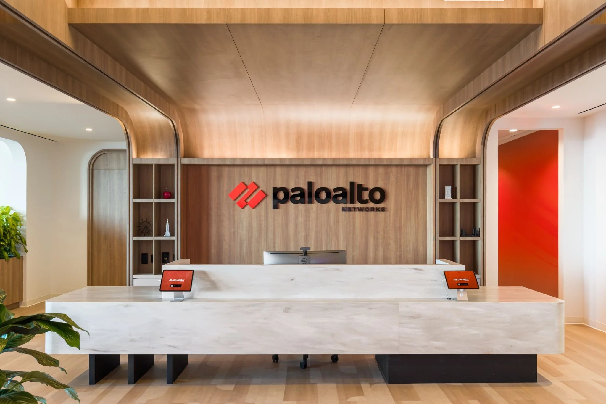 Reception area with a white marble counter, two red tablets on stands, and a wooden wall with a logo that reads 'paloalto NETWORKS'.