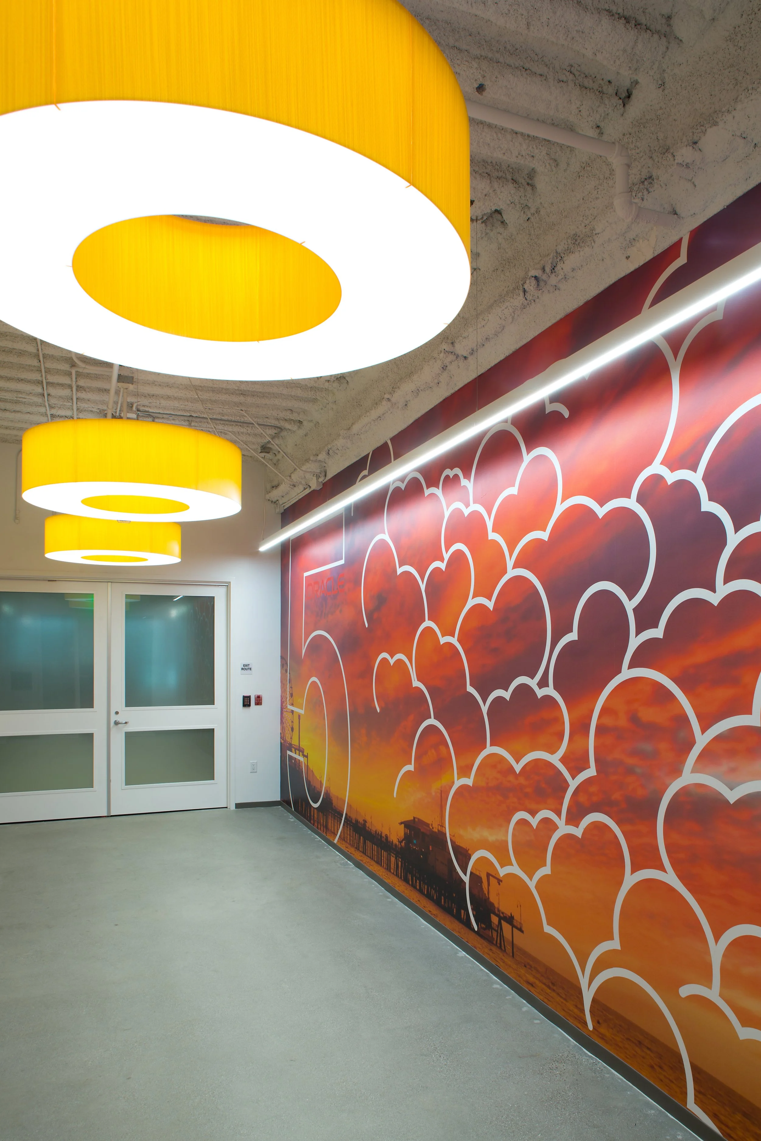 Interior space with large yellow circular ceiling lights and a mural on the wall featuring a sunset sky with clouds and a pier at sunset.