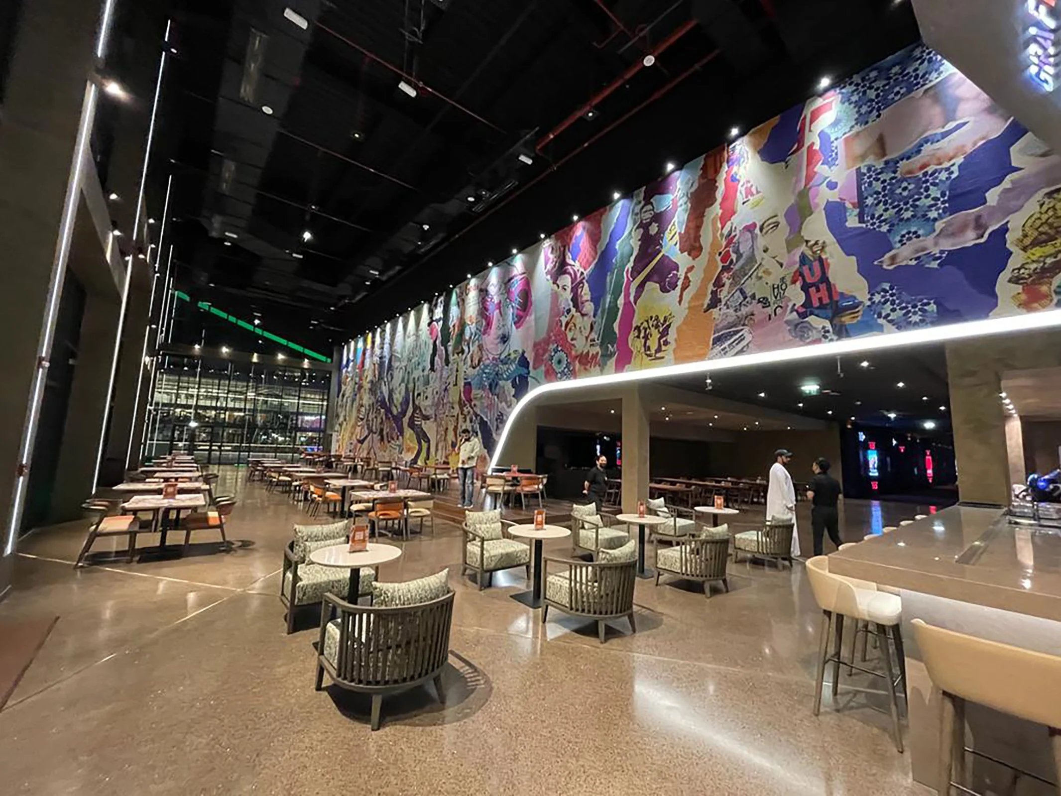 Interior of movie theater lobby with seating area, colorful wall art, and people standing and talking.