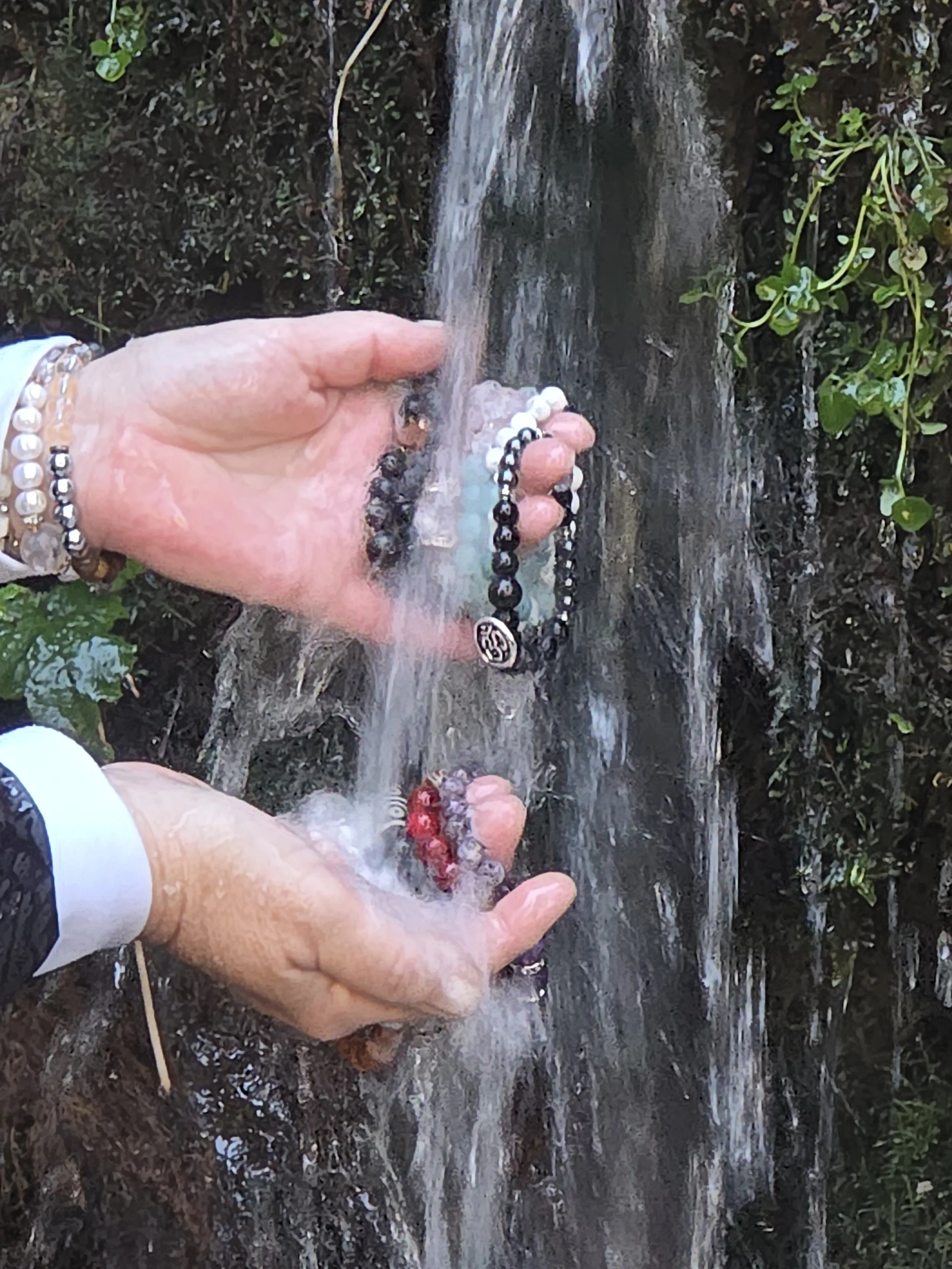 women holding handcrafted natural stone bracelets, cleansing bracelets in waterfall.
