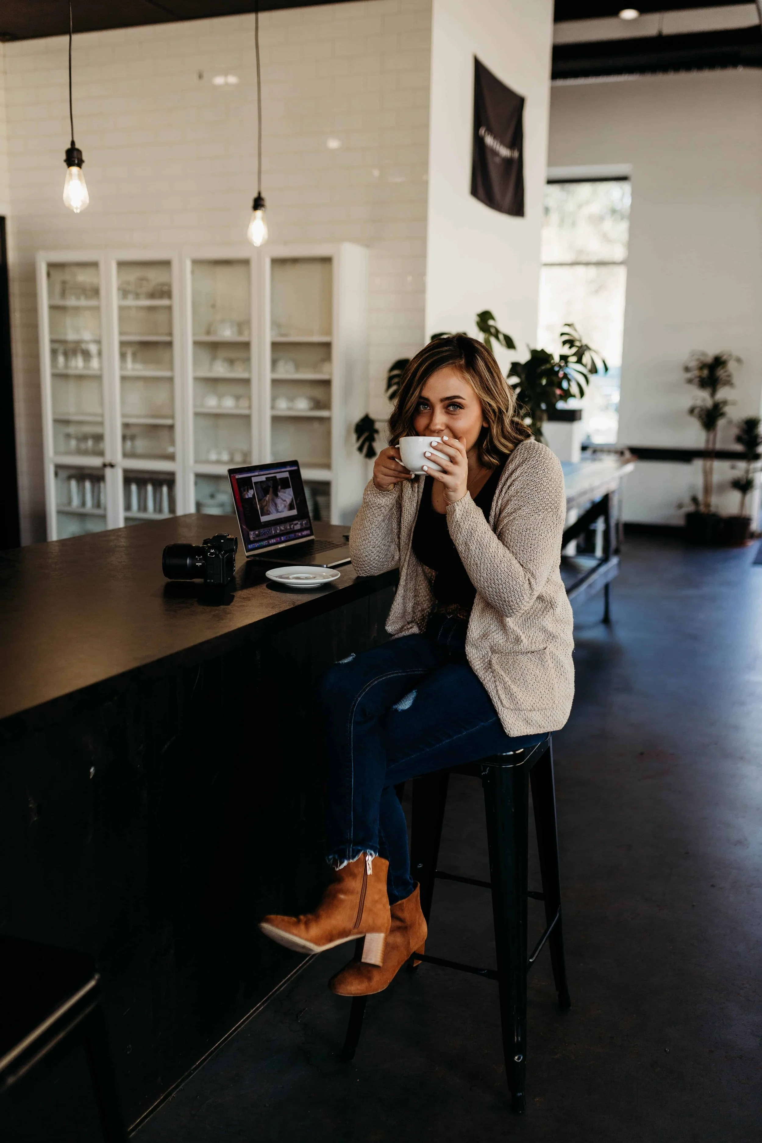 Website designer working from a modern Spokane coffee shop, sitting at a counter with a laptop, camera, and coffee