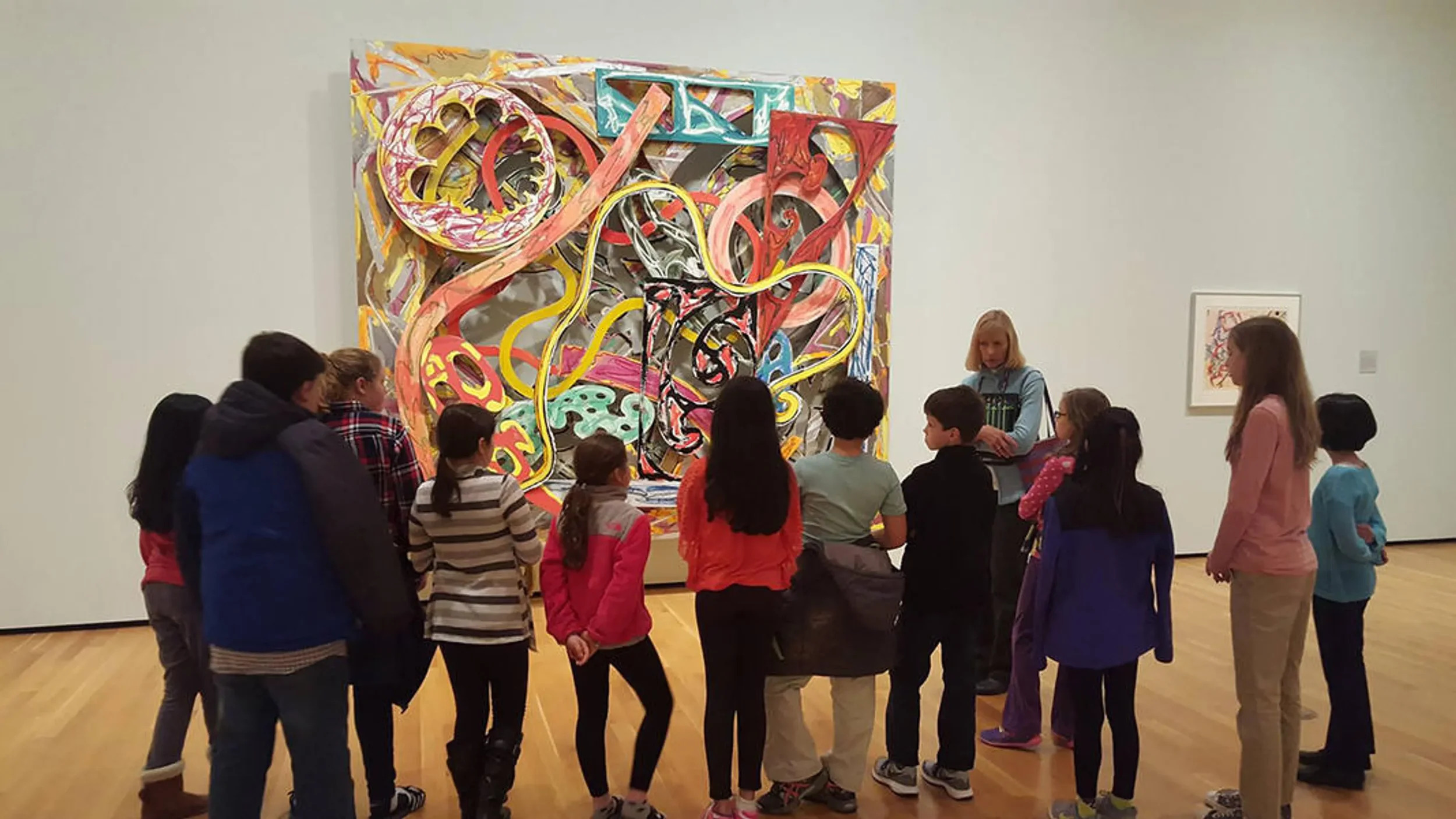 Children and adults watching a colorful abstract painting in an art gallery.