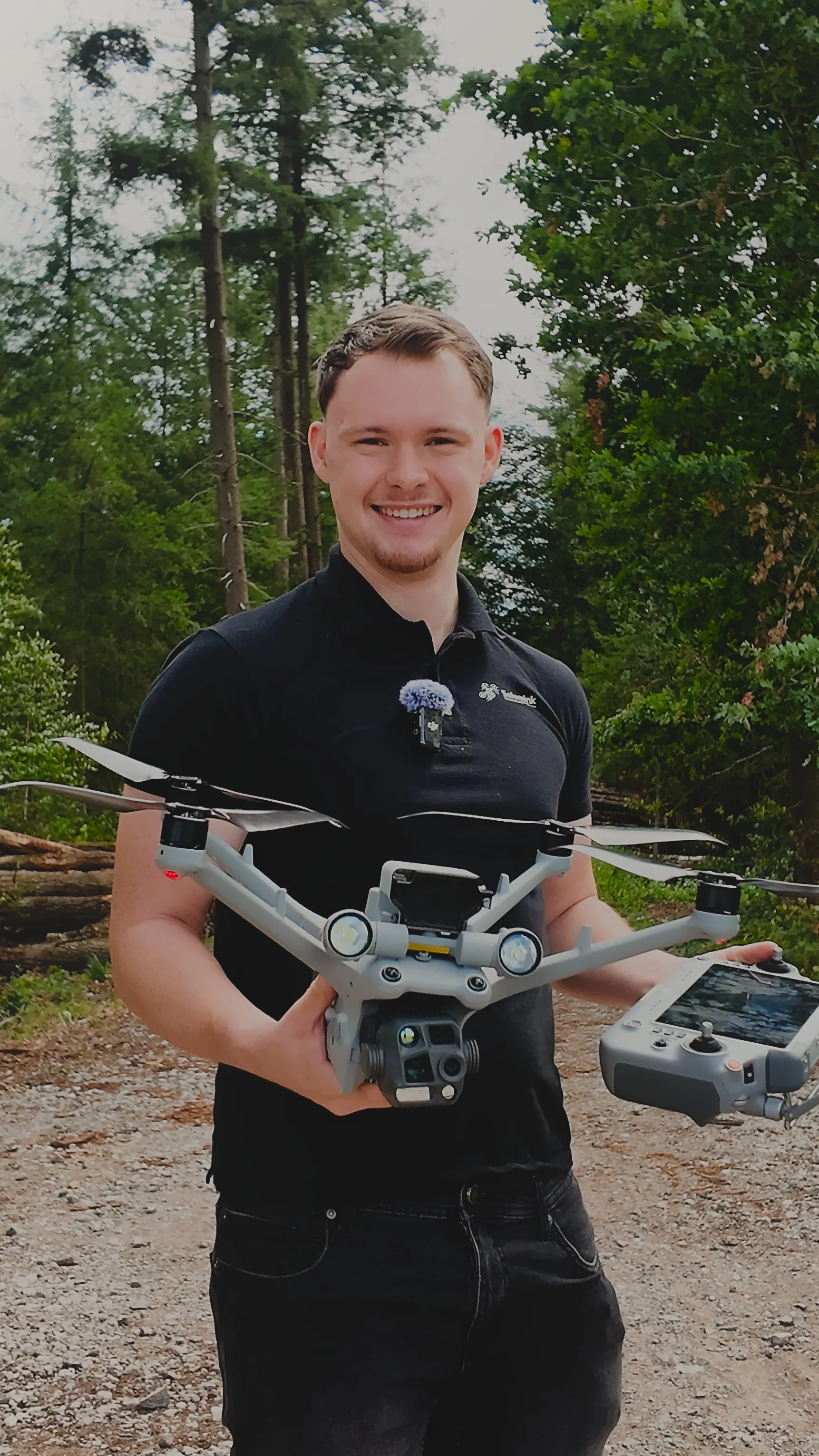 Ein junger Mann hält eine Drohne mit einem Controller in einem Wald im Freien.