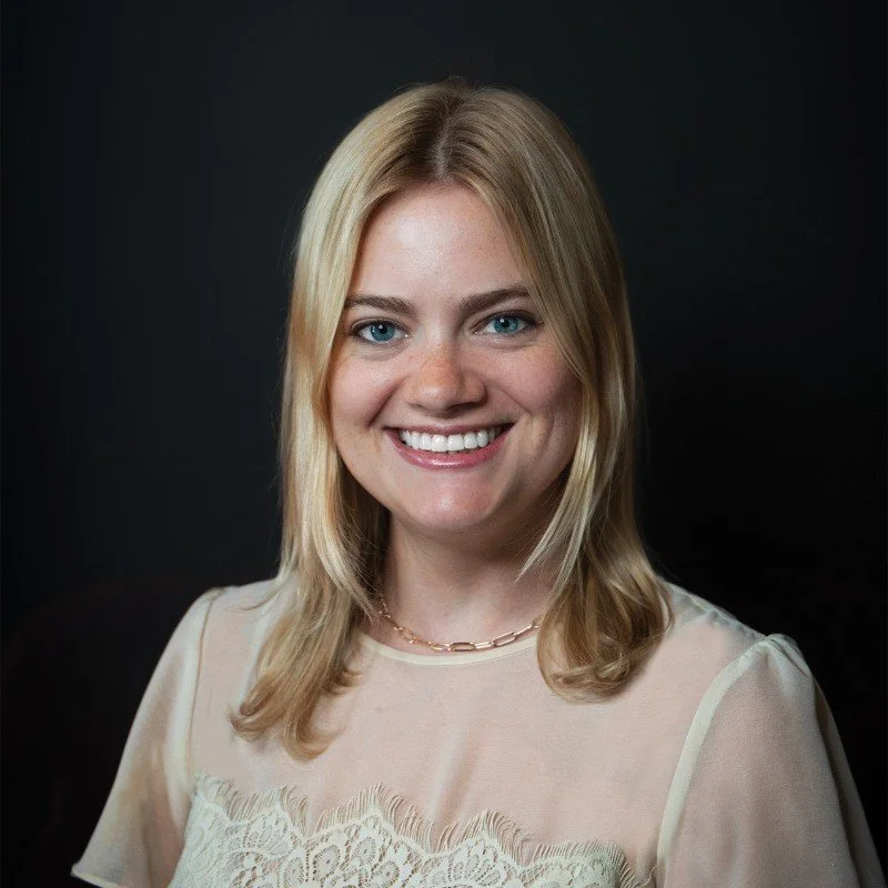 Portrait of a young woman with blonde hair smiling against a dark background.
