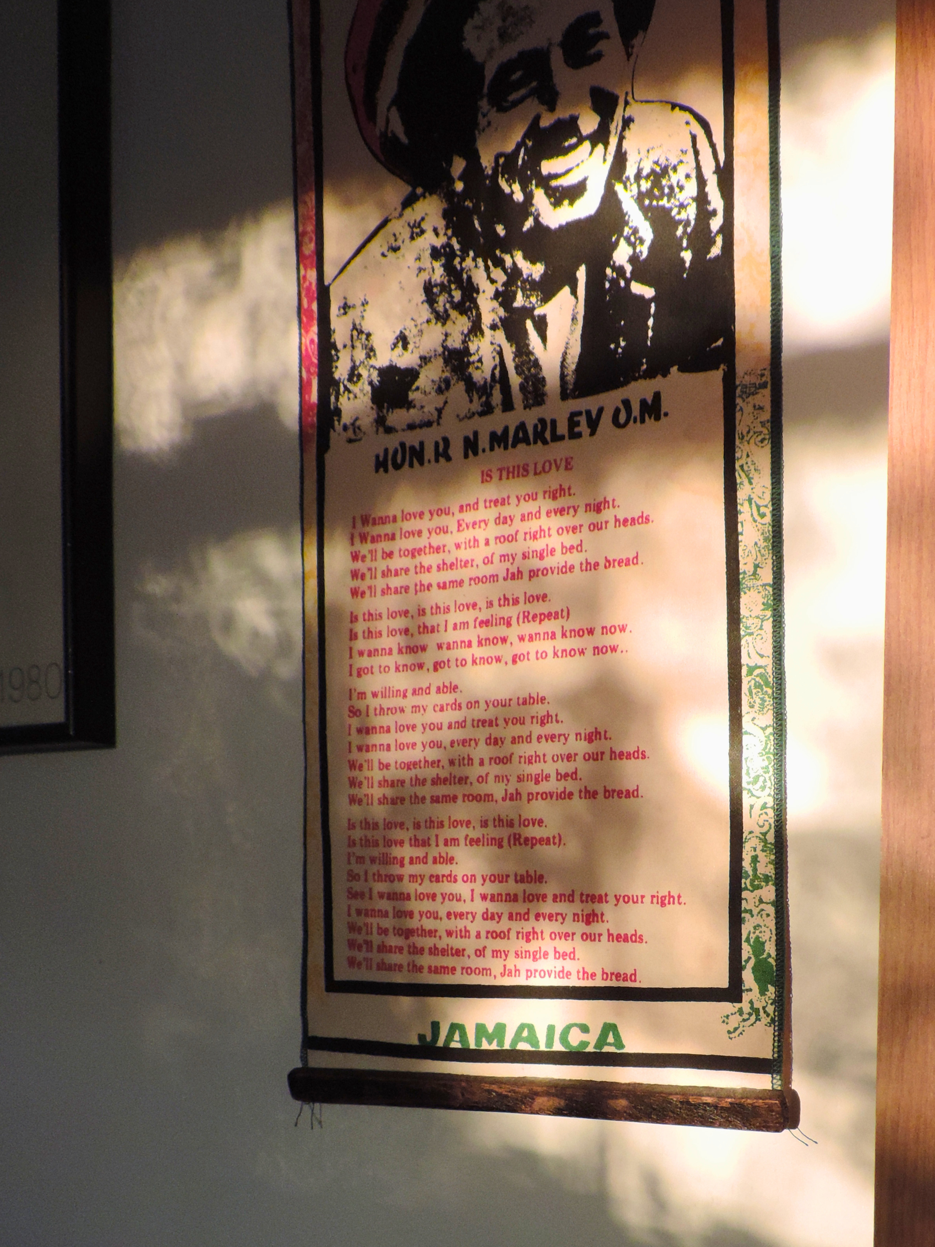A poster on a wall with the image of Bob Marley and Jamaica written at the bottom, along with a poem or song lyrics in red and black text.