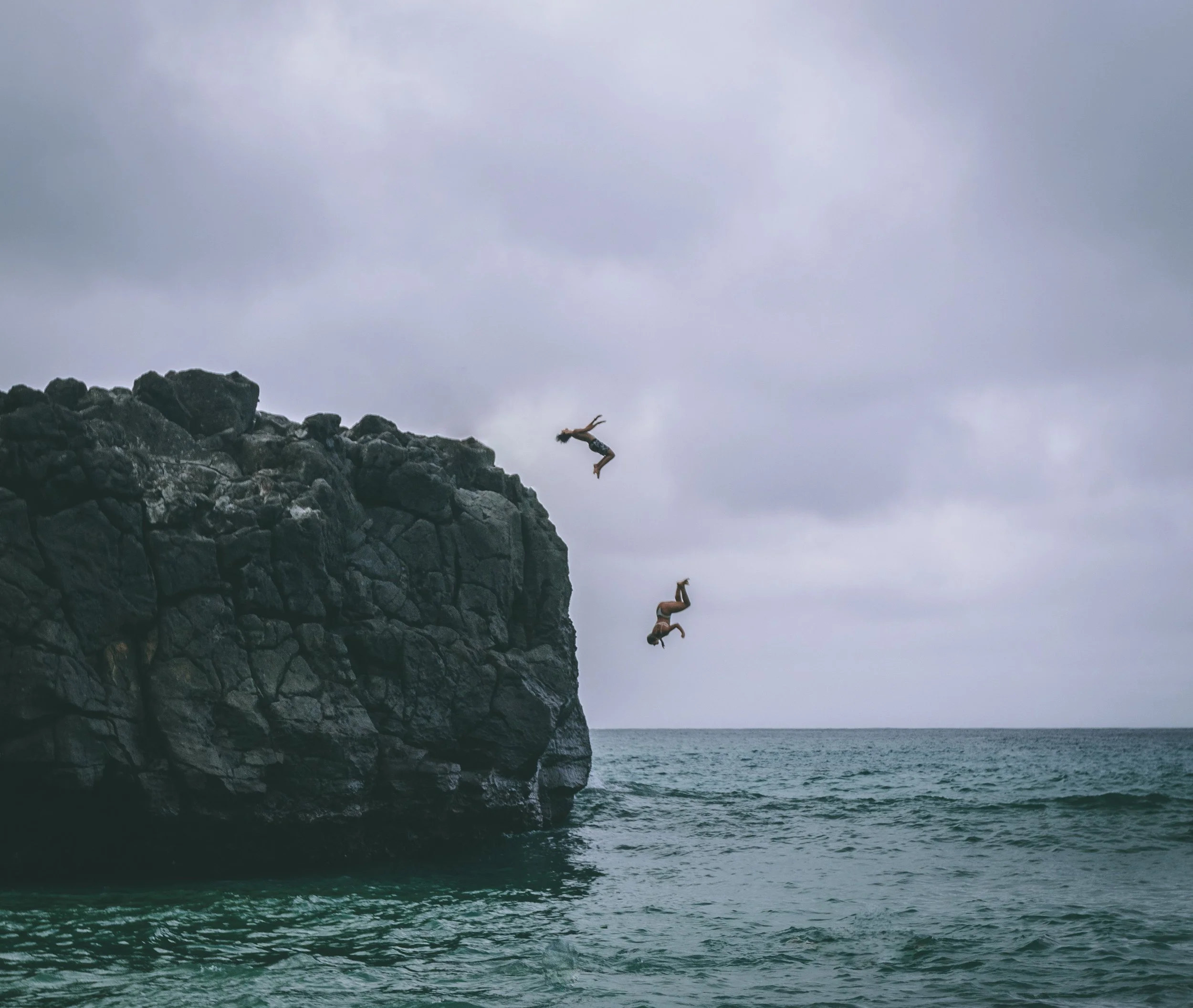 two people diving off of a cliff into the sea