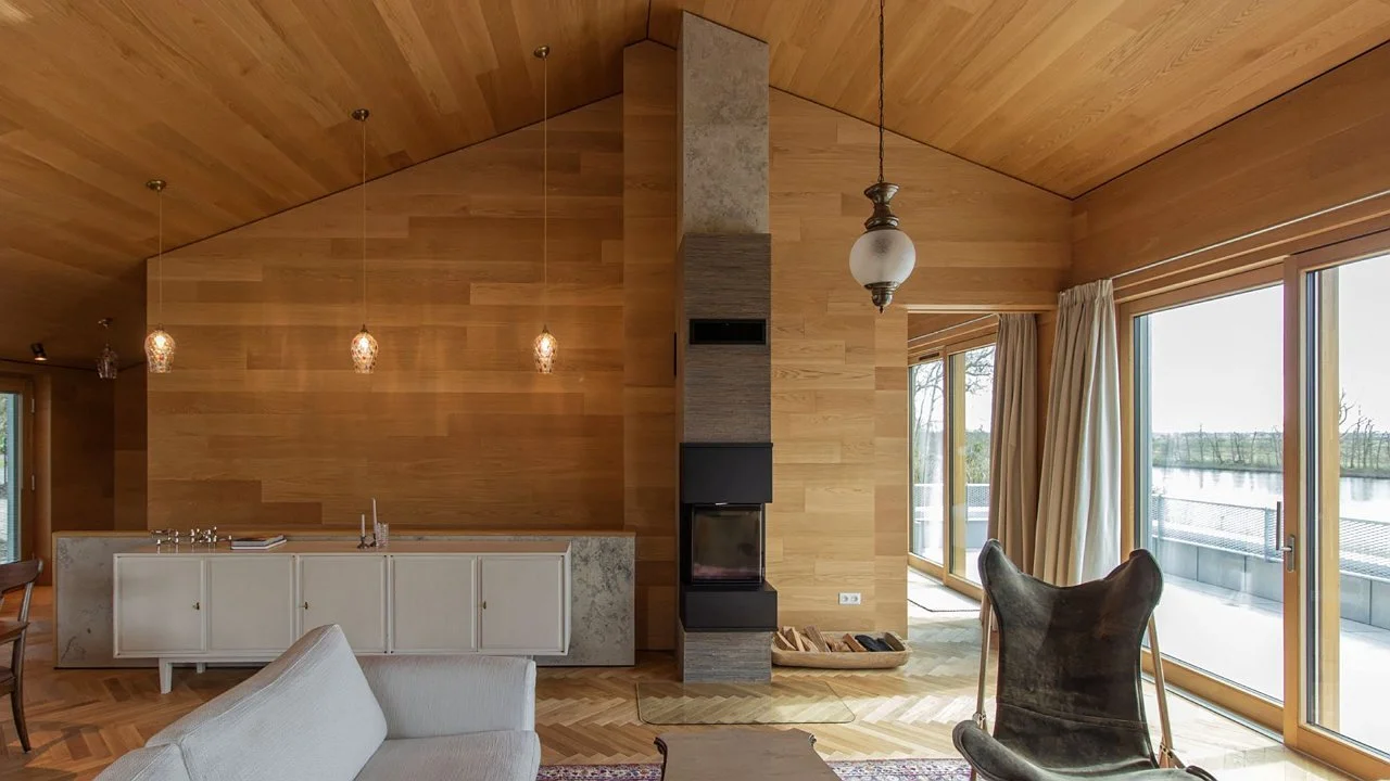 Interior of a modern living space with wooden walls, a fireplace, large windows with curtains, and stylish chairs.