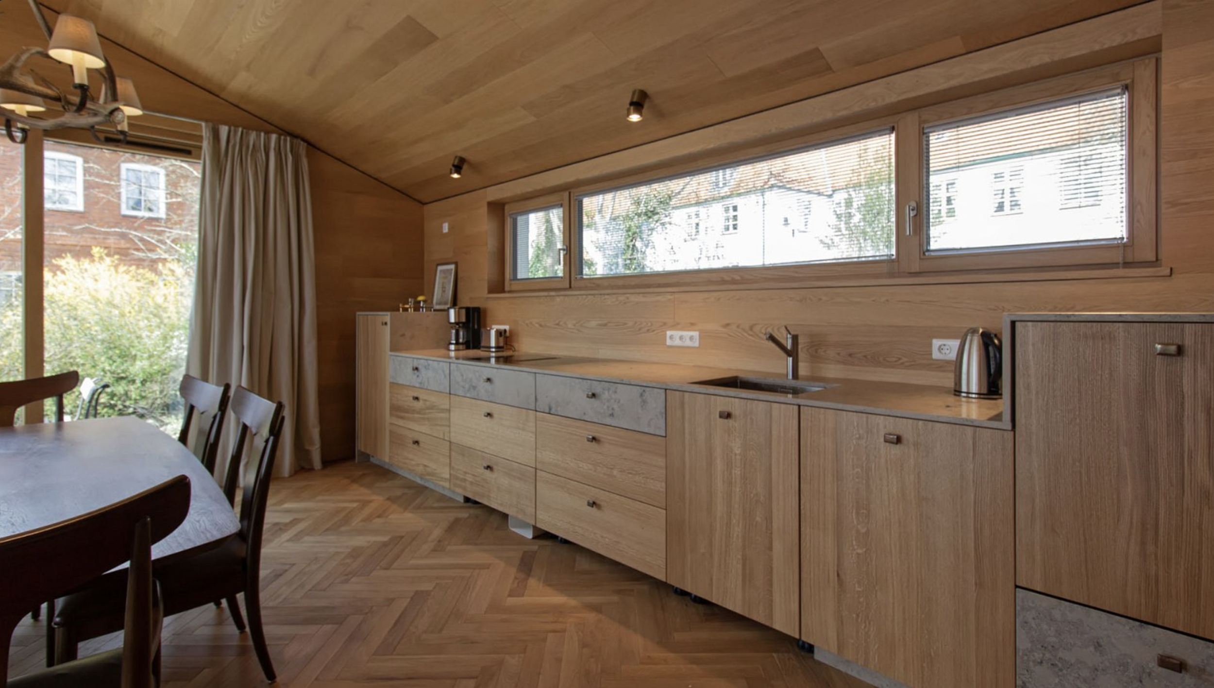 Kitchen with wooden cabinets, a large window, a coffee maker, a kettle, and a set of drawers, with a dining table and chairs nearby.
