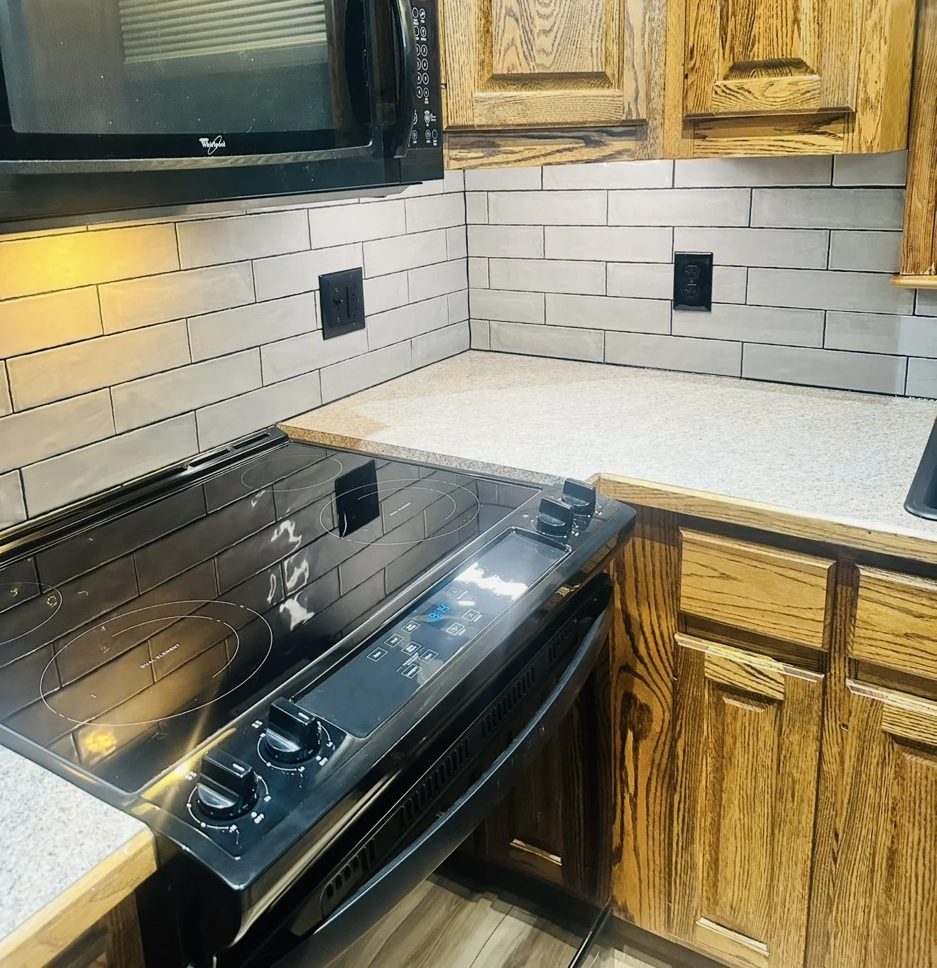 Kitchen with wood cabinets, a black electric stovetop, a microwave, and a tiled backsplash.