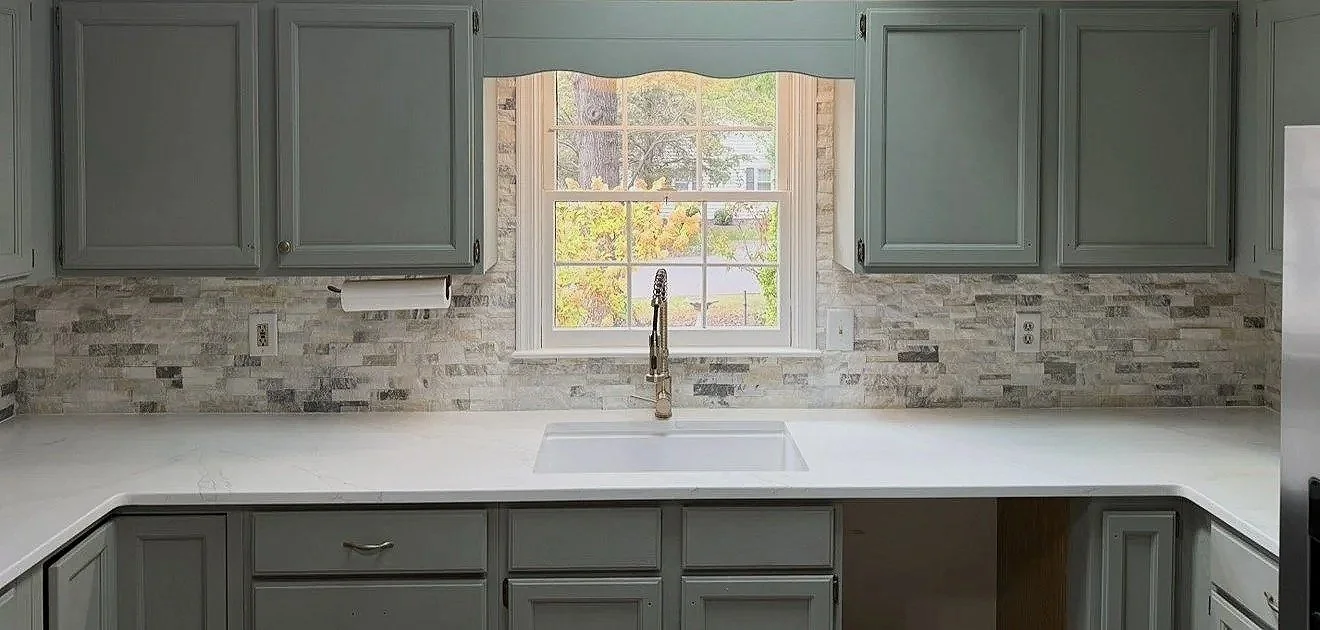Kitchen with gray cabinets, a white countertop, a window above the sink, and a brick backsplash.
