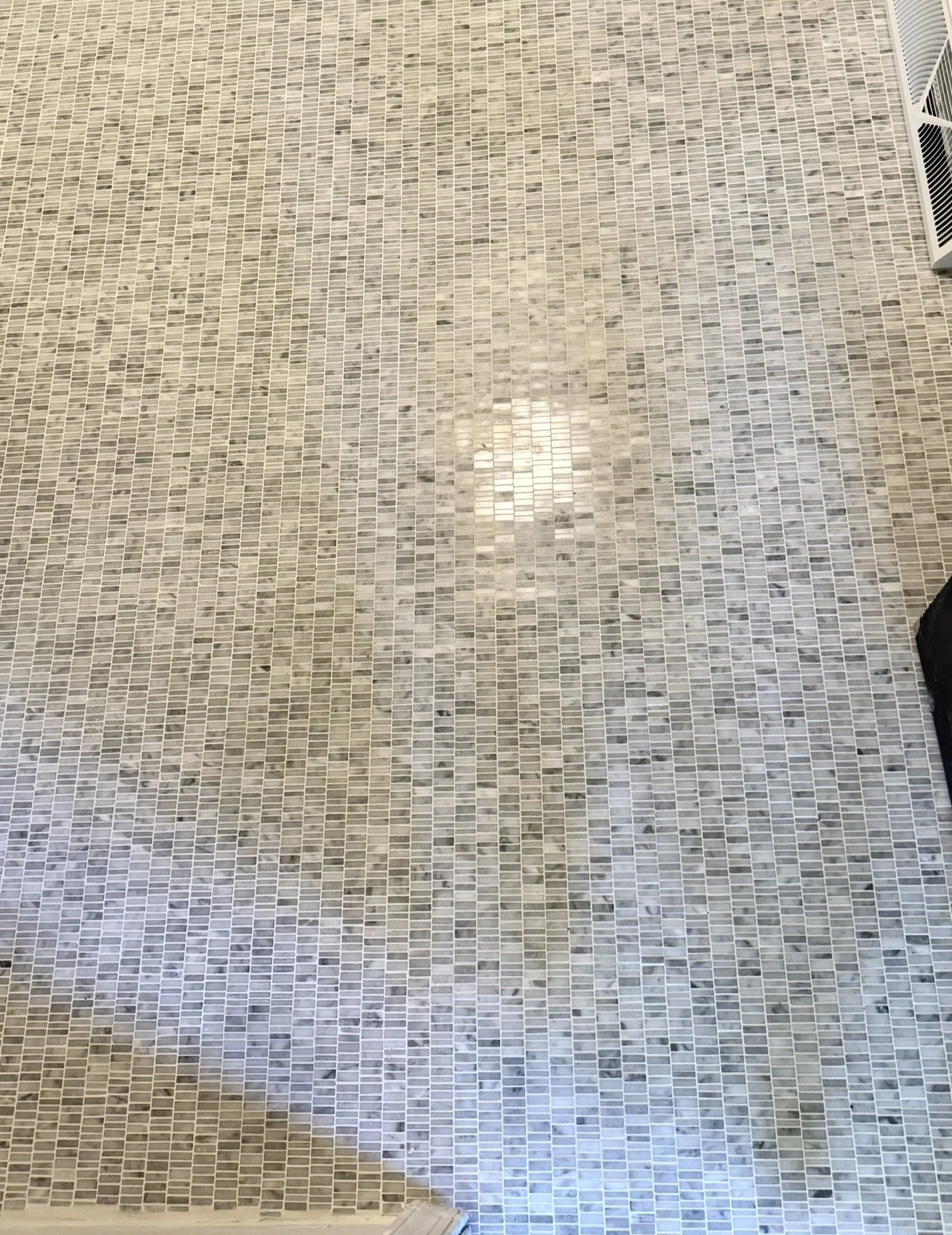 Close-up of a tiled bathroom floor with small rectangular mosaic tiles in shades of gray and white.