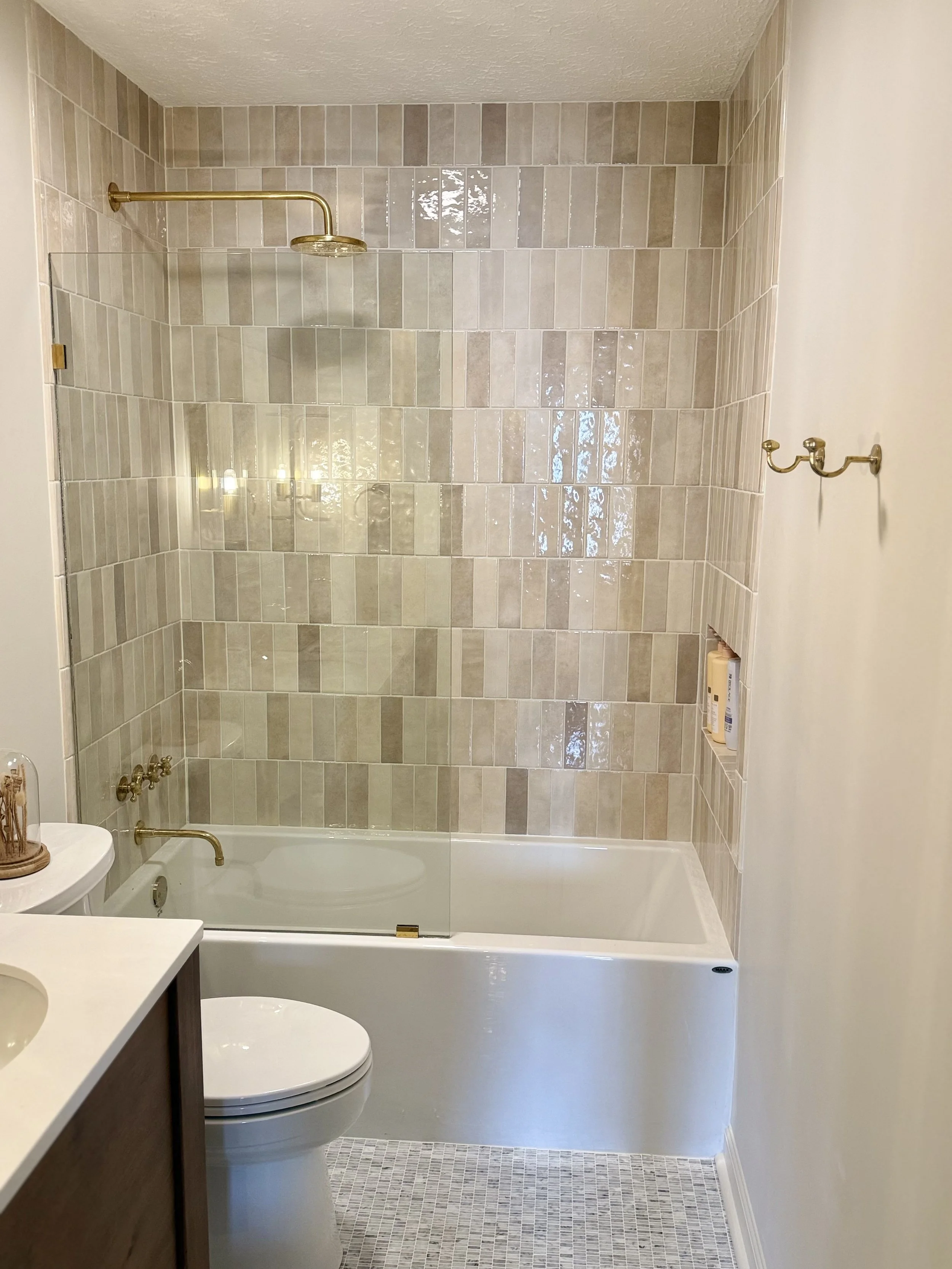 Bathroom with beige tiled shower area, brass fixtures, glass shower door, toilet, and sink with dark wood cabinet.