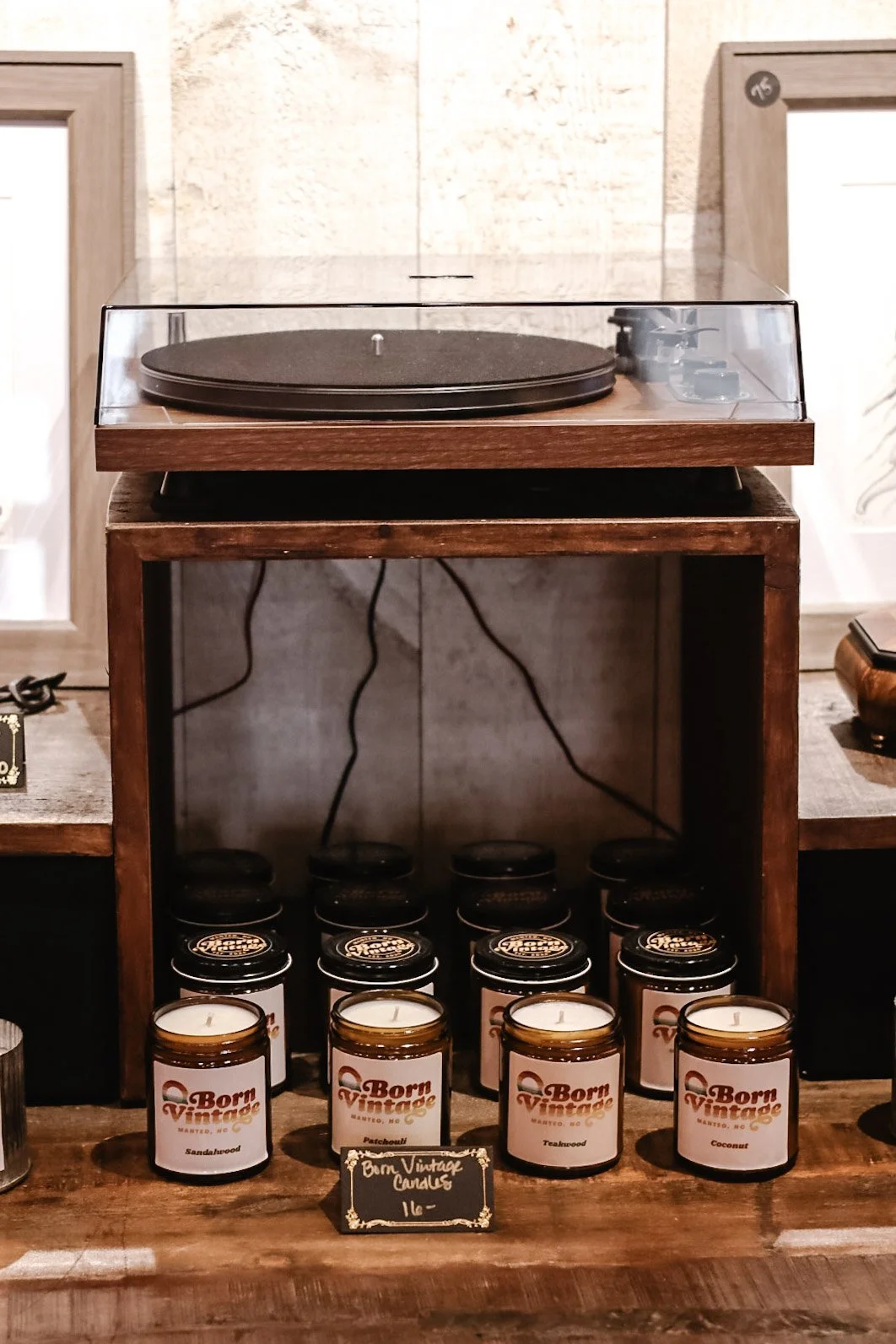 Vintage turntable on wooden stand with candles labeled 'Born Vintage' below, against a brick wall background.