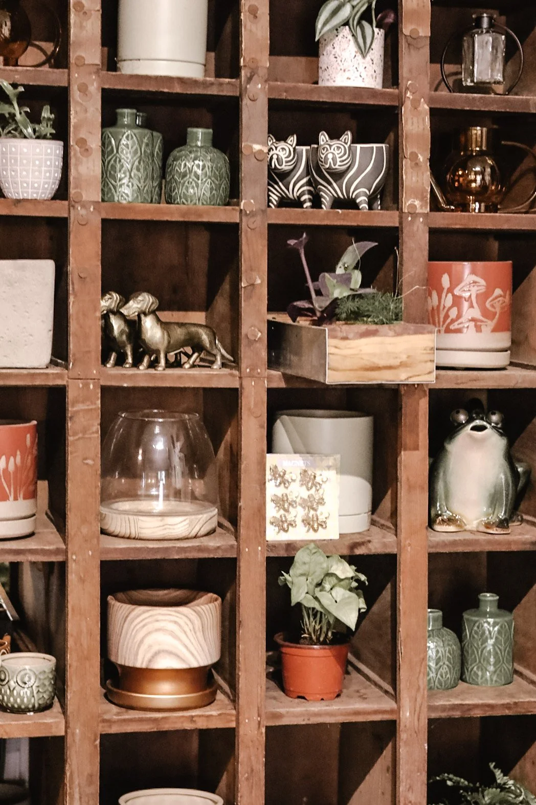 A wooden shelving unit filled with various decorative items, including ceramic vases, pots, small statues, plants, and other ornaments.