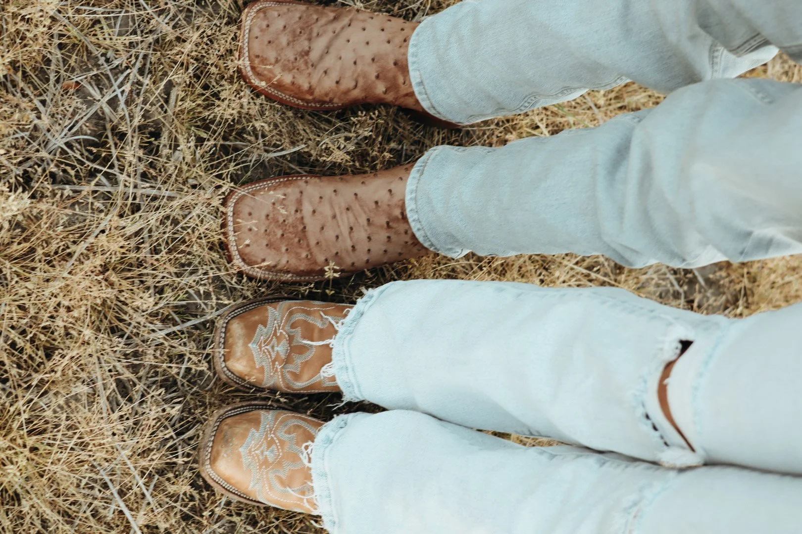 Person wearing cowboy boots on dry grass.